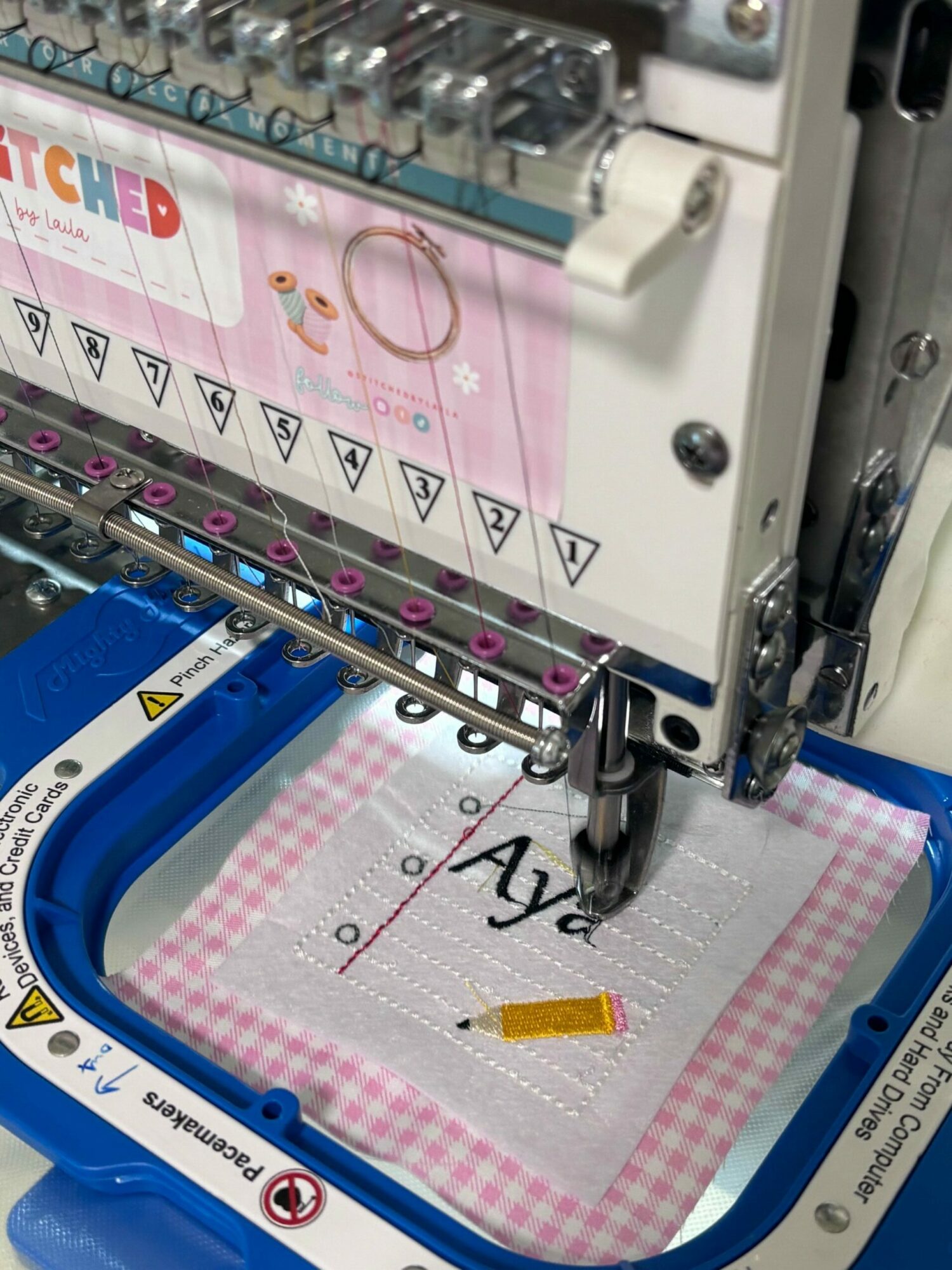 Sewing machine with fabric and a needle, partially visible, with a blue and pink checkered fabric in the hoop.