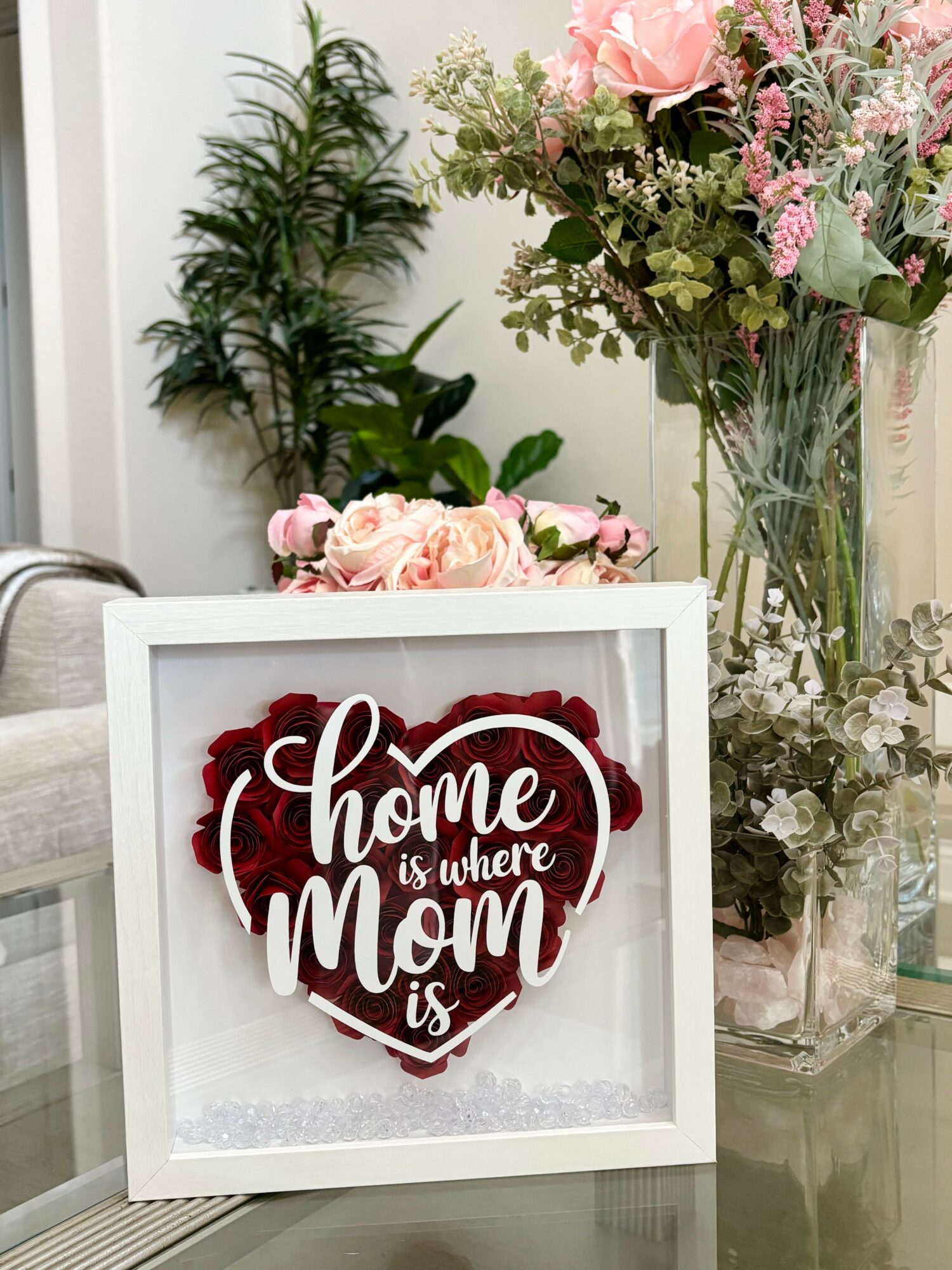Decorative framed sign with a heart and the text 'home is where mom is' surrounded by flowers.