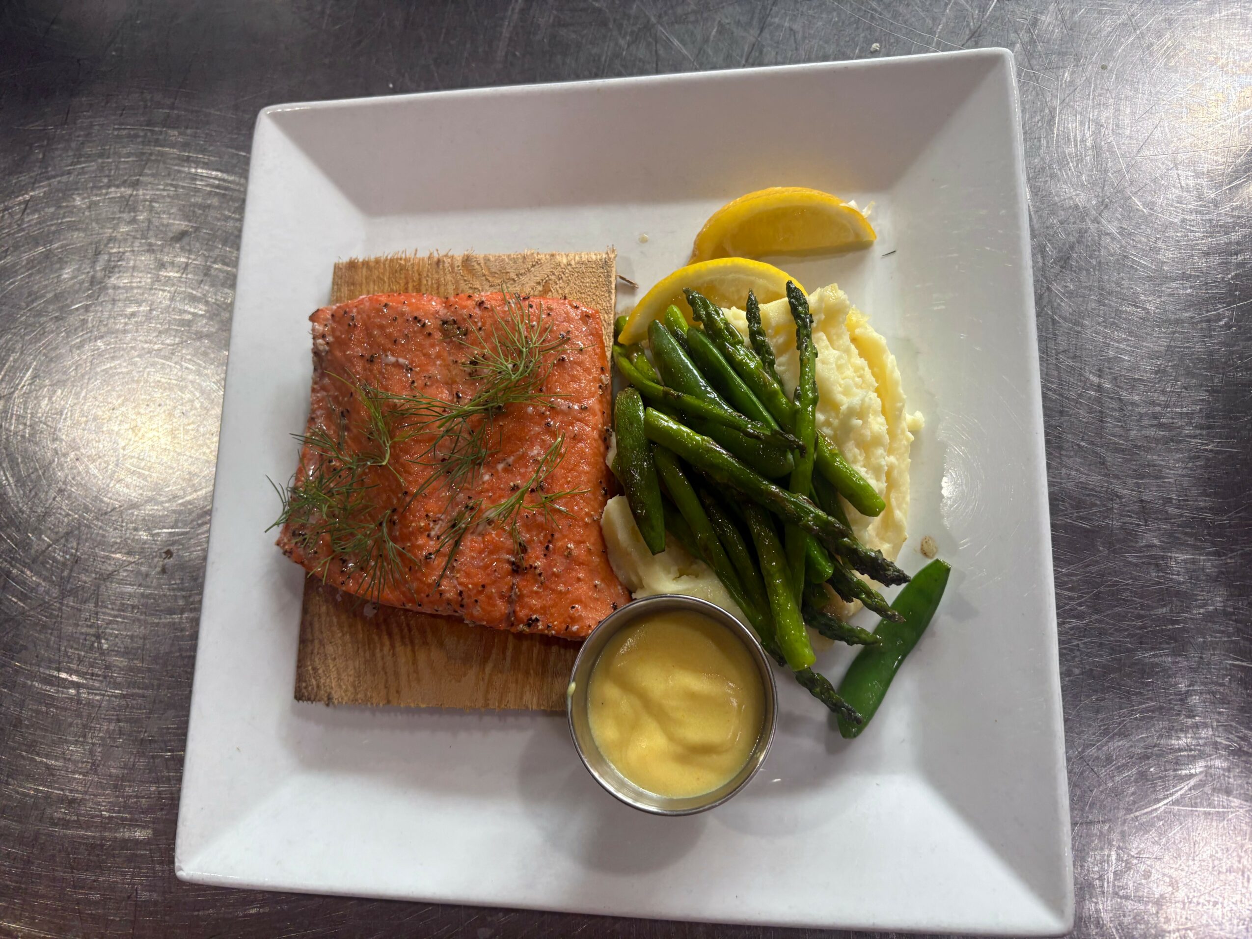 Plate with breaded fish, green beans, mashed potatoes, lemon wedge, and mustard sauce on a white square plate.