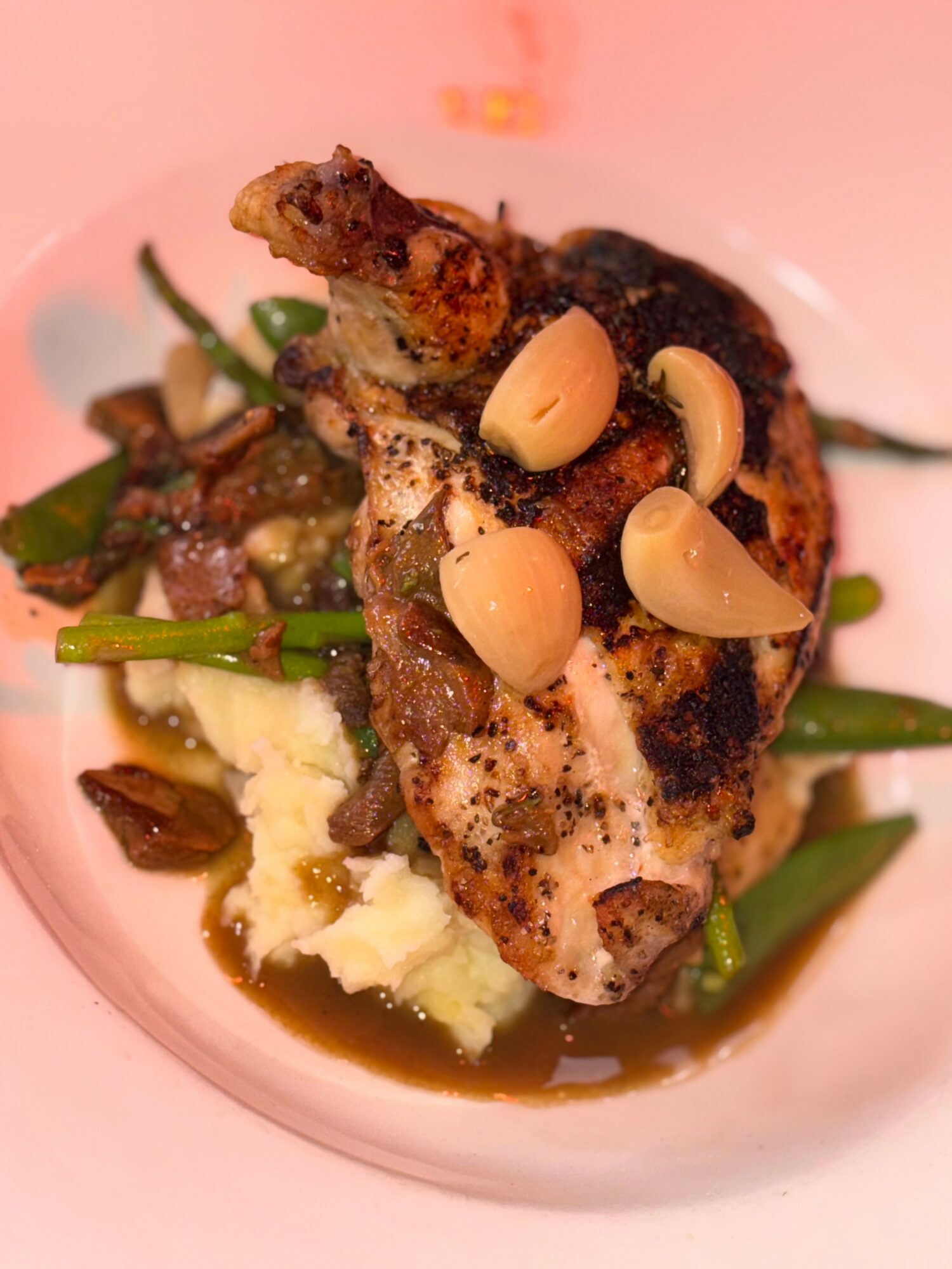 Grilled chicken leg with garlic cloves, green beans, and mashed potatoes on a plate.