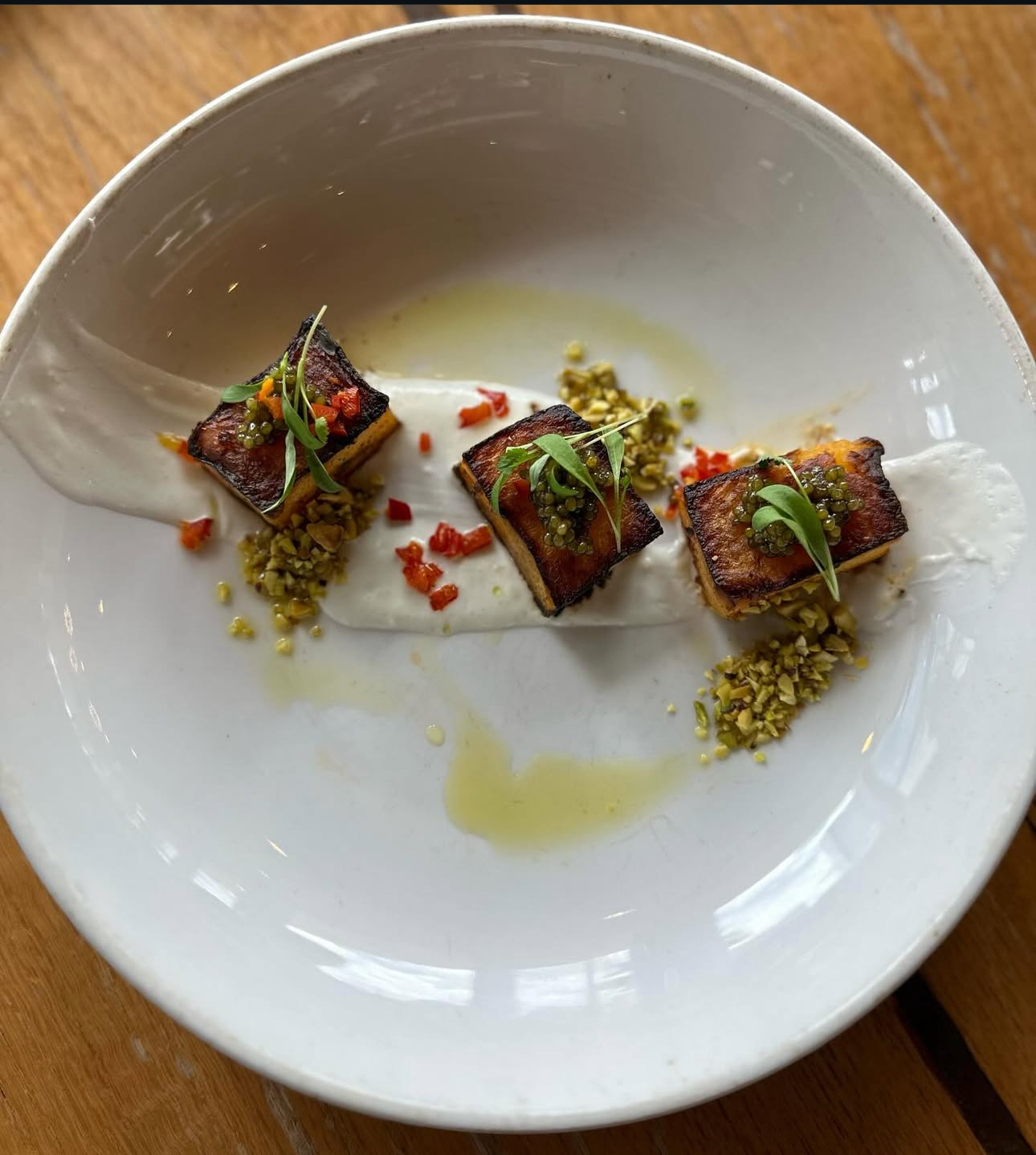 Three small, rectangular pieces of food garnished with herbs and spices on a white plate with sauce and crushed toppings.