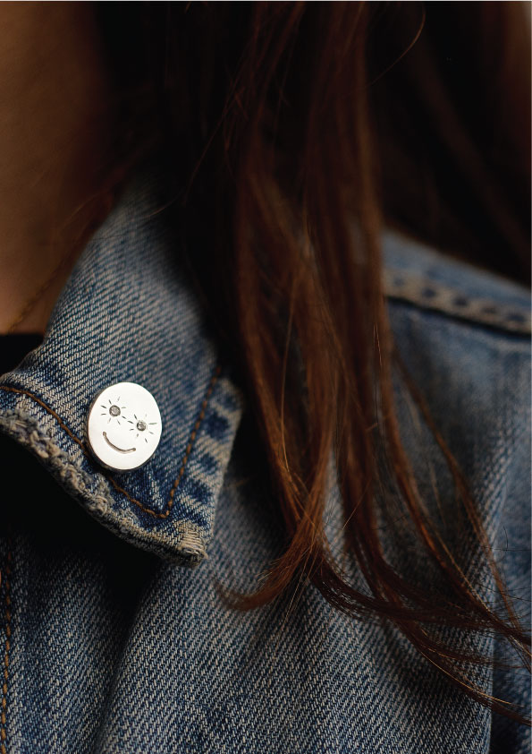 Close-up of denim jacket with a smiley face pin and brown hair.