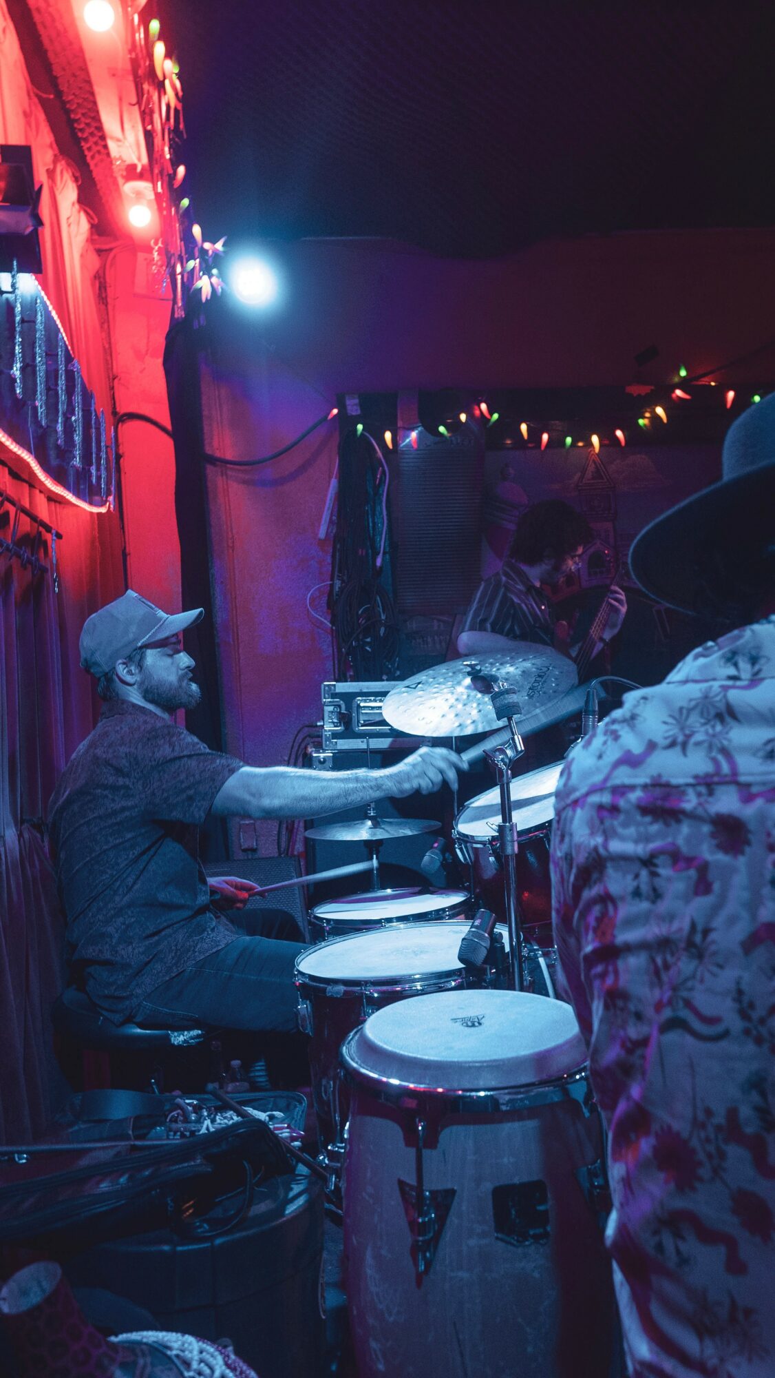 Musicians playing drums and percussion at a lively indoor event with colorful lights and decorations.