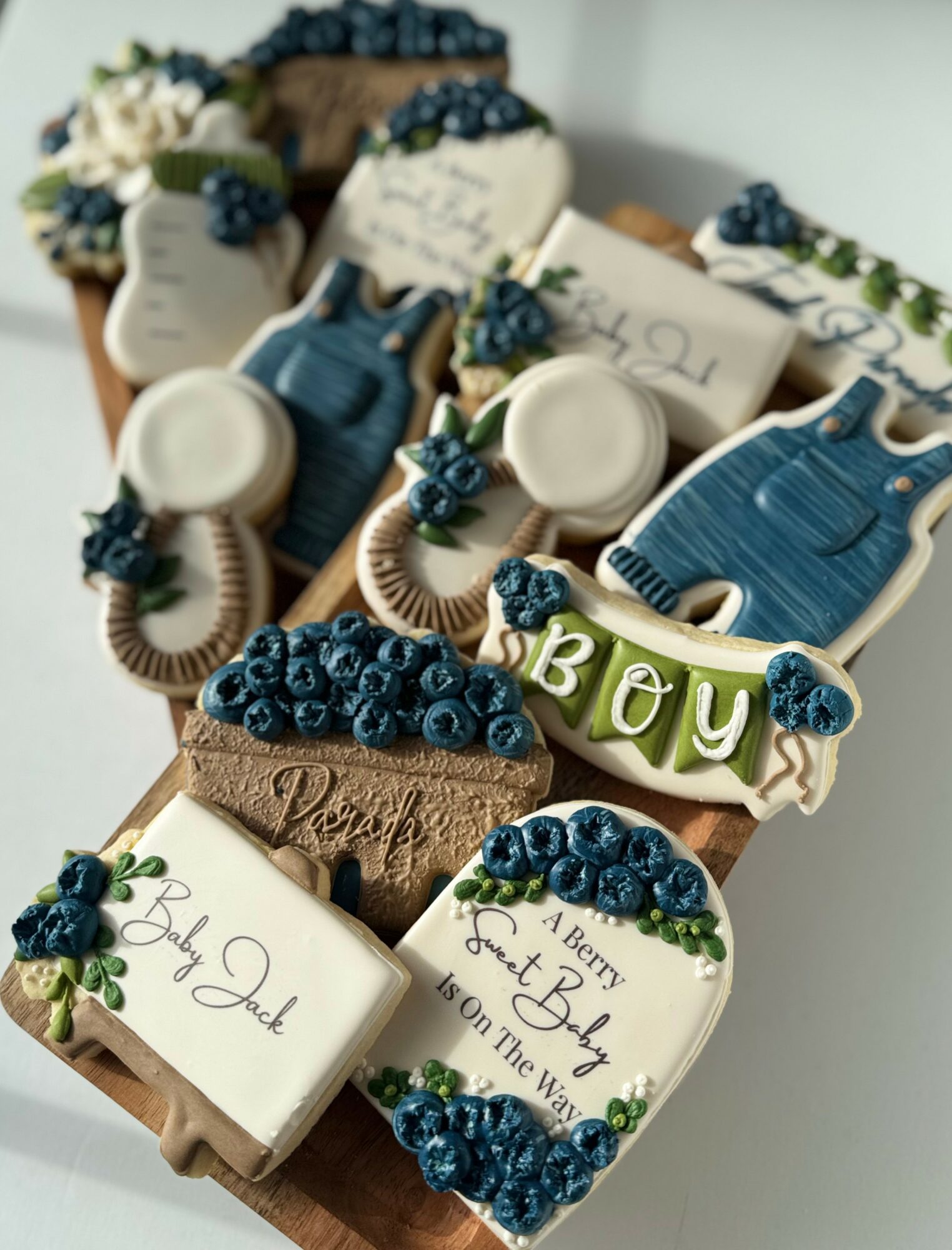 Decorative cookies with blue and white themes, including a boy-themed cookie, arranged on a wooden board.