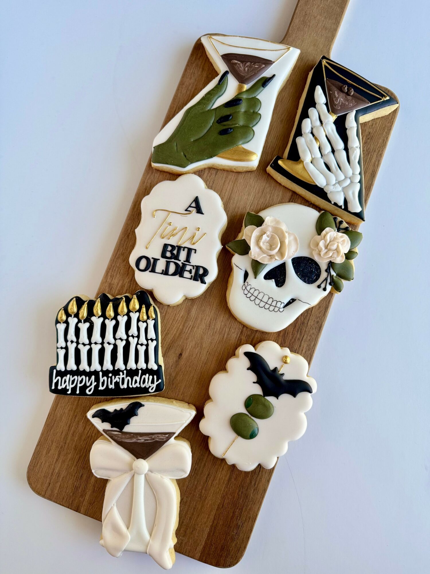 Assorted decorated cookies on a wooden tray, including a skull with flowers, a bat, and birthday messages.