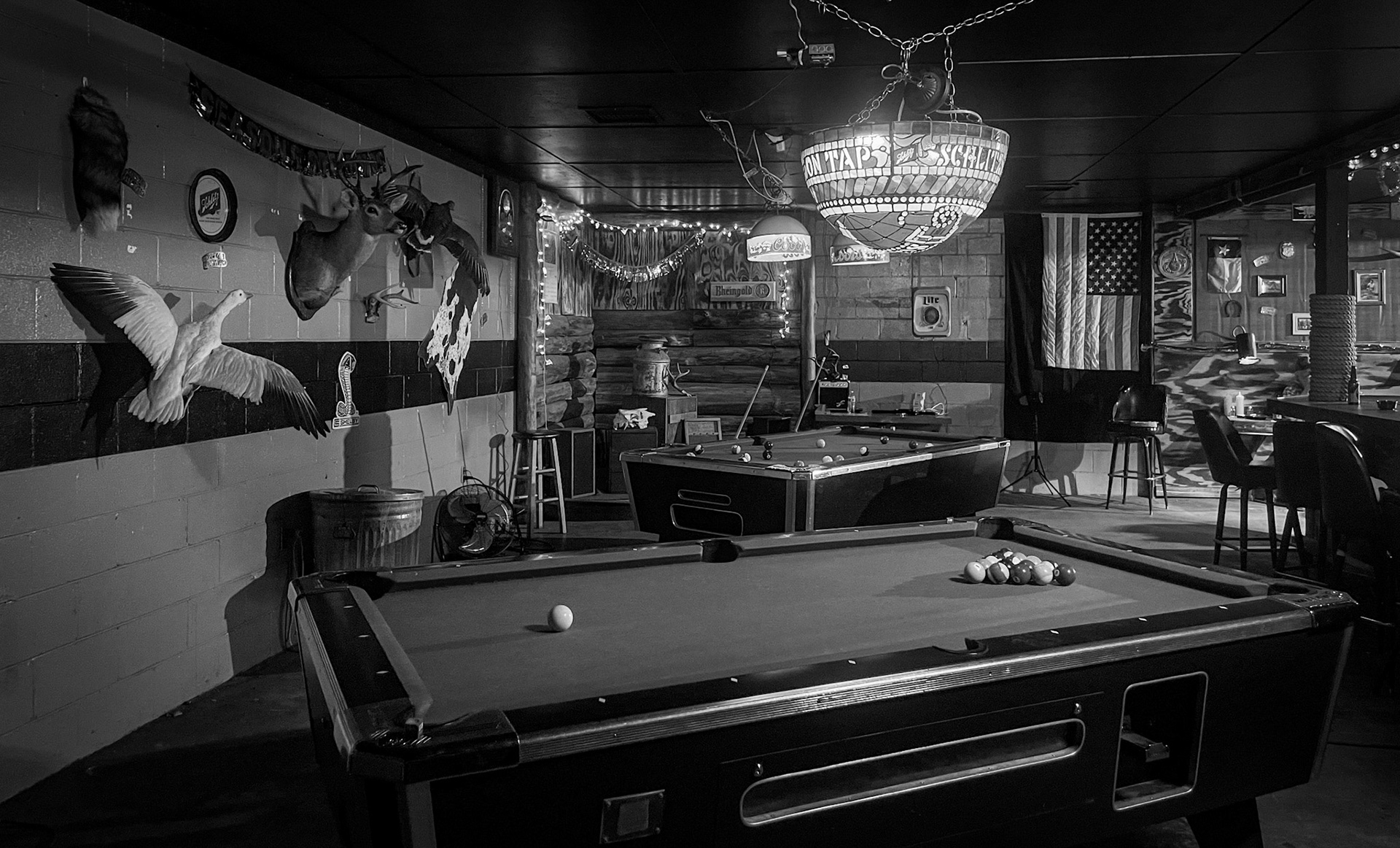 Pool table with balls, chandelier, mural, and seating area in a dimly lit room.