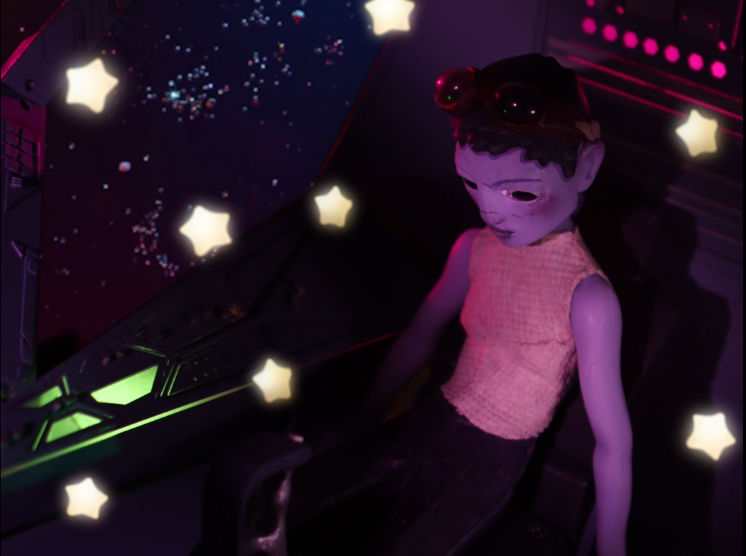 A child-like figure with dark hair and a pink top sits in a dark environment with glowing star-shaped lights around.