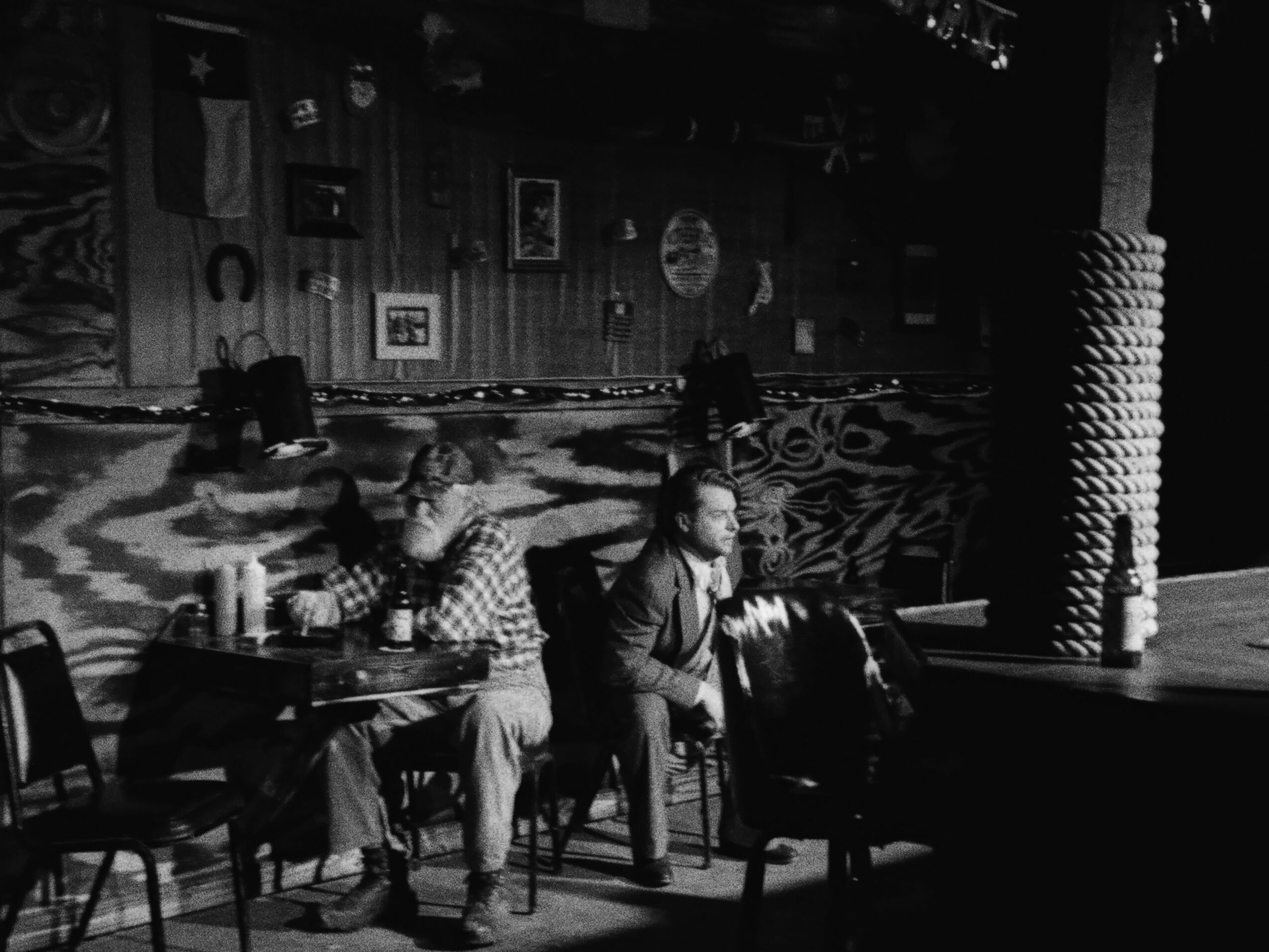 People sitting at tables in a dimly lit room with patterned carpet and wall decorations.