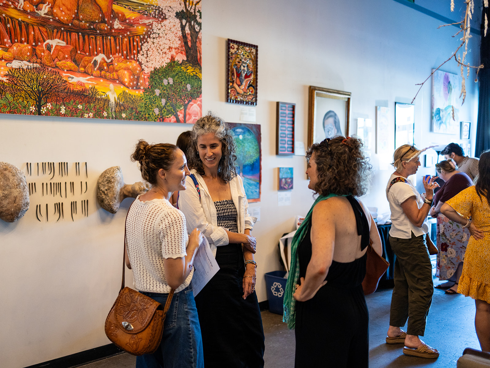People viewing artwork in an art gallery, with paintings and framed pieces on the wall.