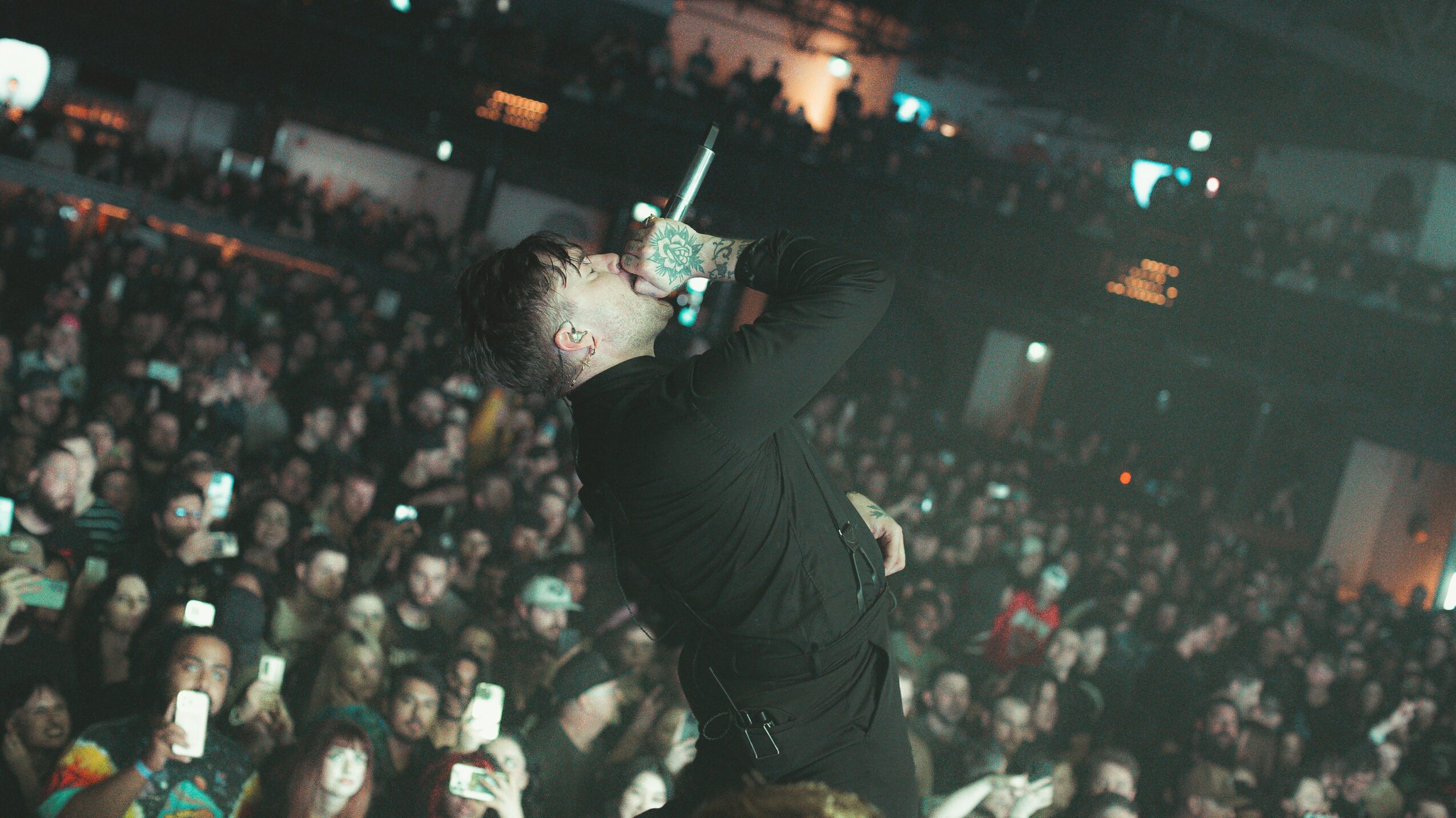 Performer singing into a microphone on stage with a large audience in the background.