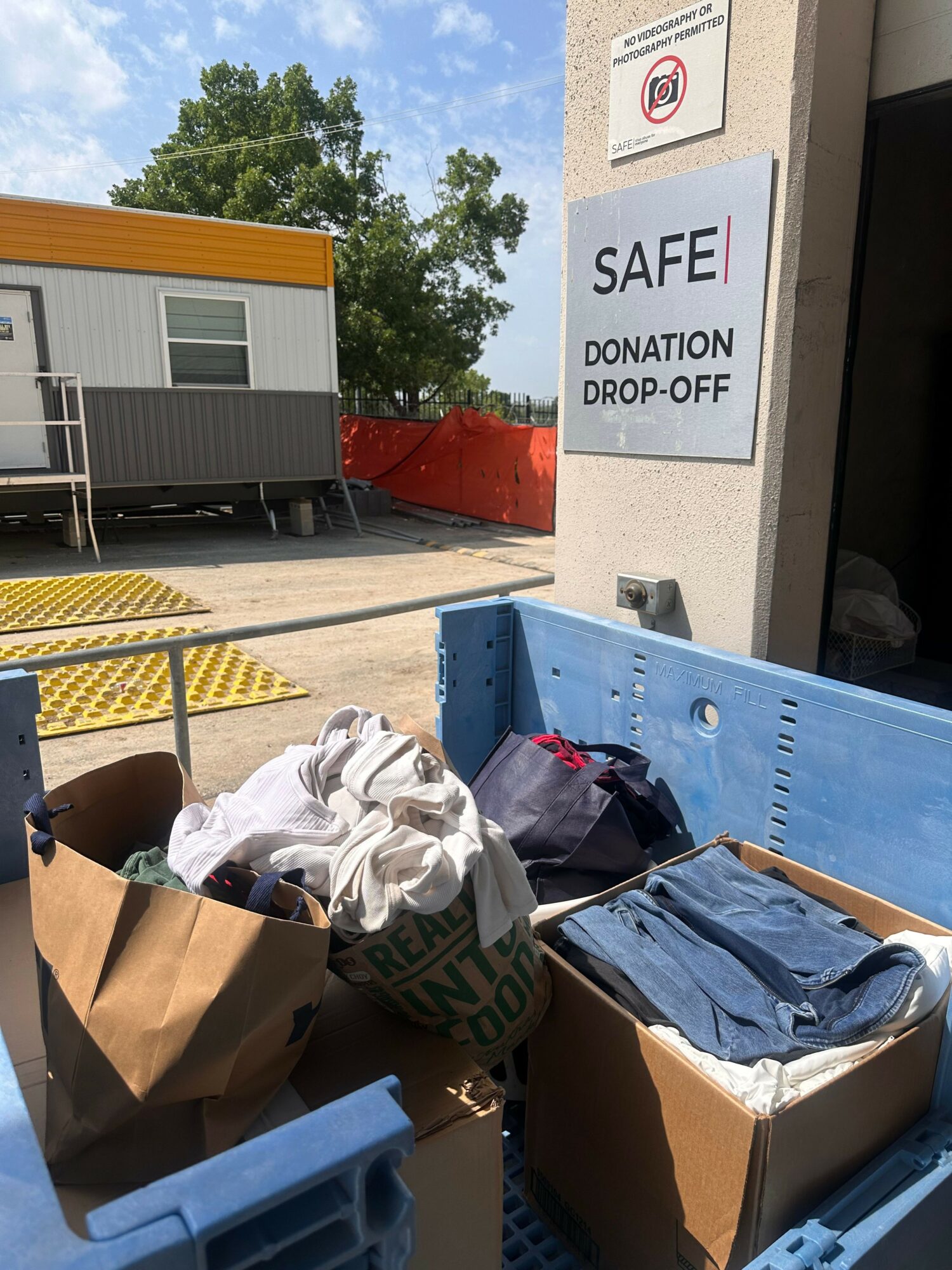 Table with donation items, boxes, and a sign that says 'SAFE DONATION DROP OFF' outside a building.