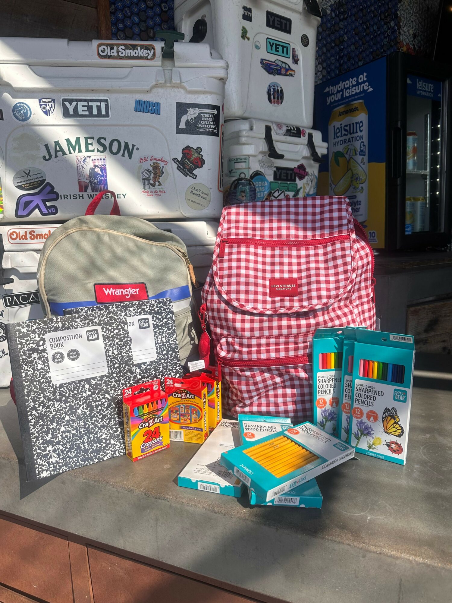 Display of various school supplies, including a red and white checkered backpack, notebooks, and stationery items on a table.