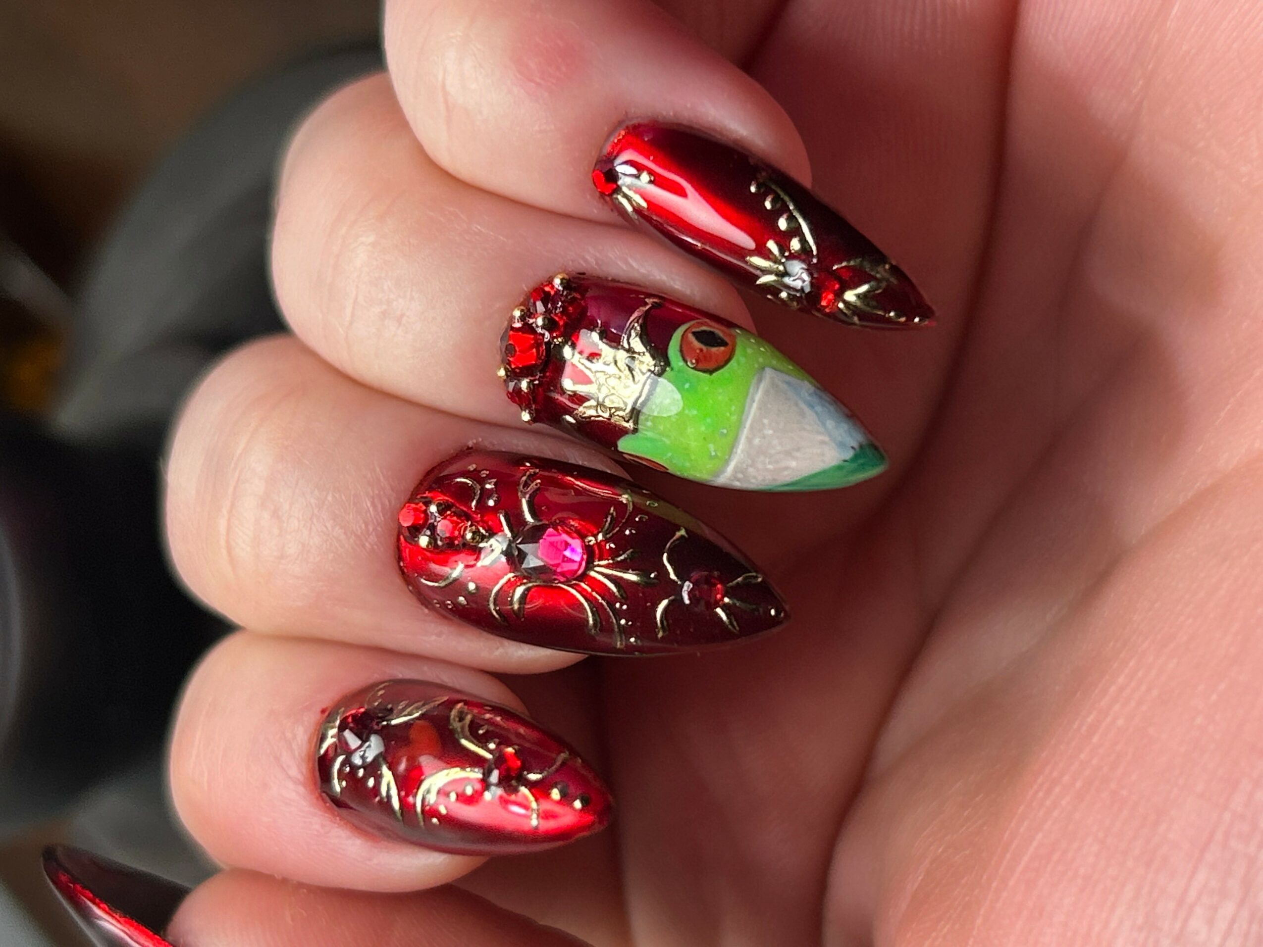 Hand with decorated Christmas-themed nails, including a green and white elf face, red and gold designs, and rhinestones.