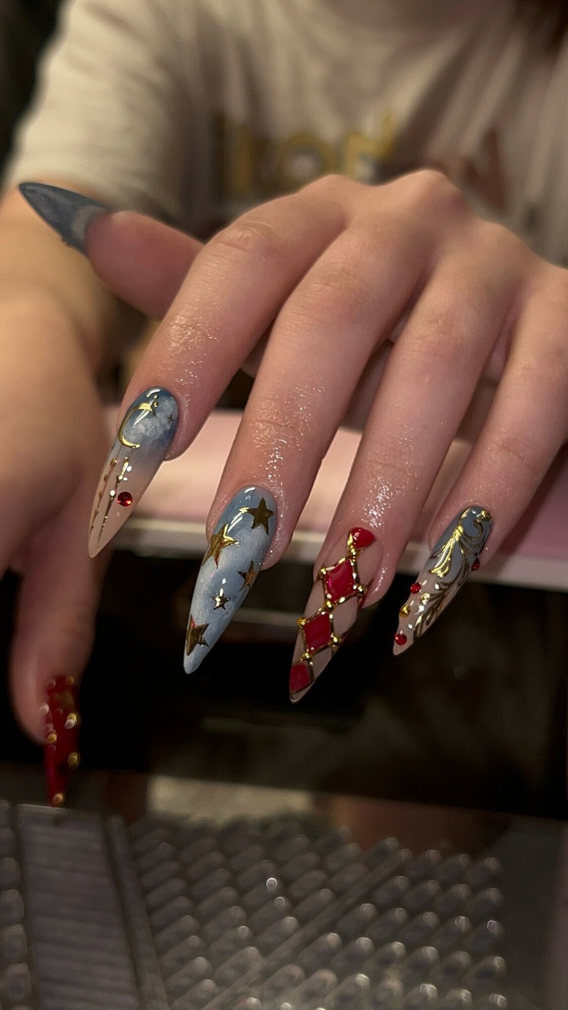 Hand with long, decorated nails featuring Christmas-themed designs, including stars, snowflakes, and red and gold accents.