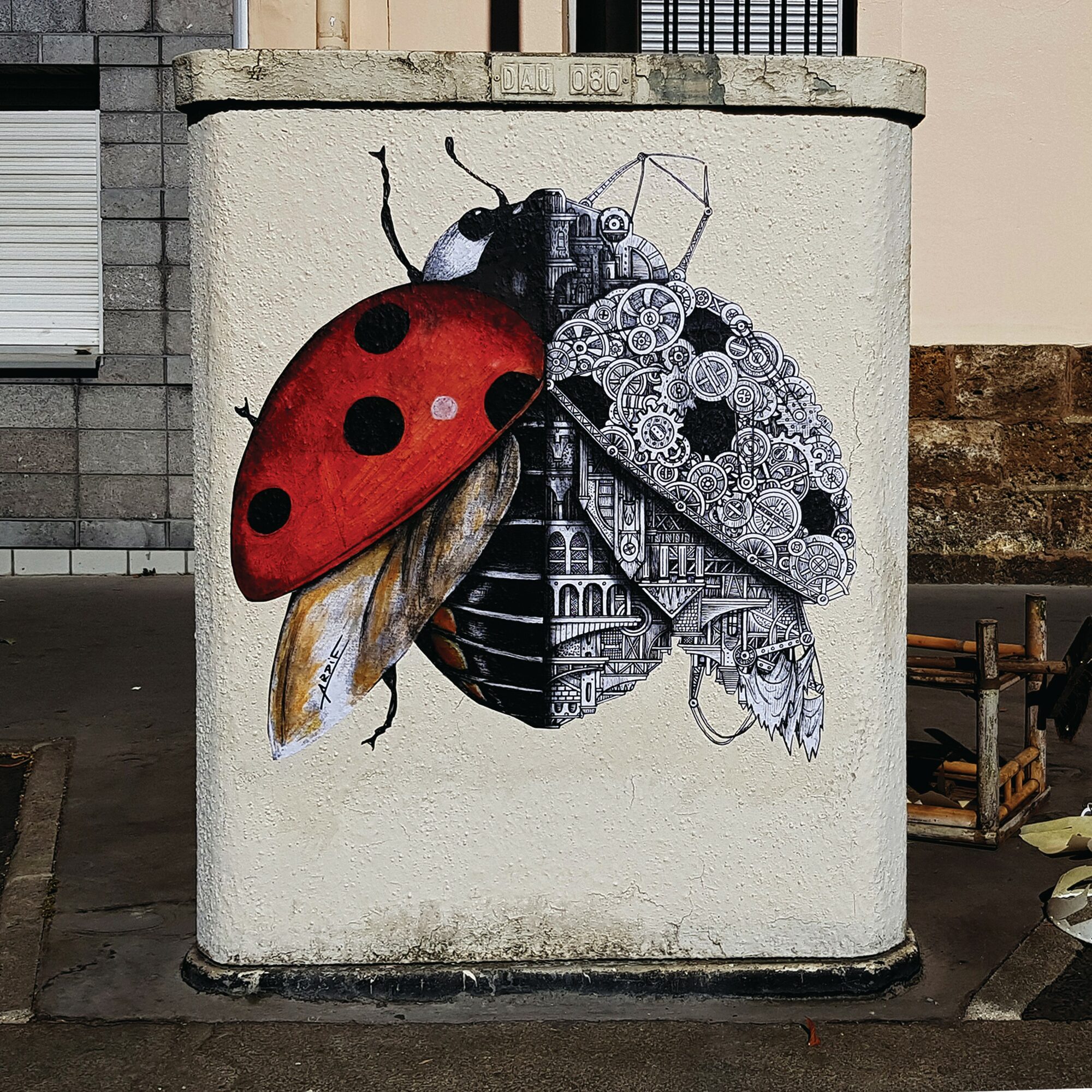 Street art of a ladybug with mechanical and architectural elements on a white wall.