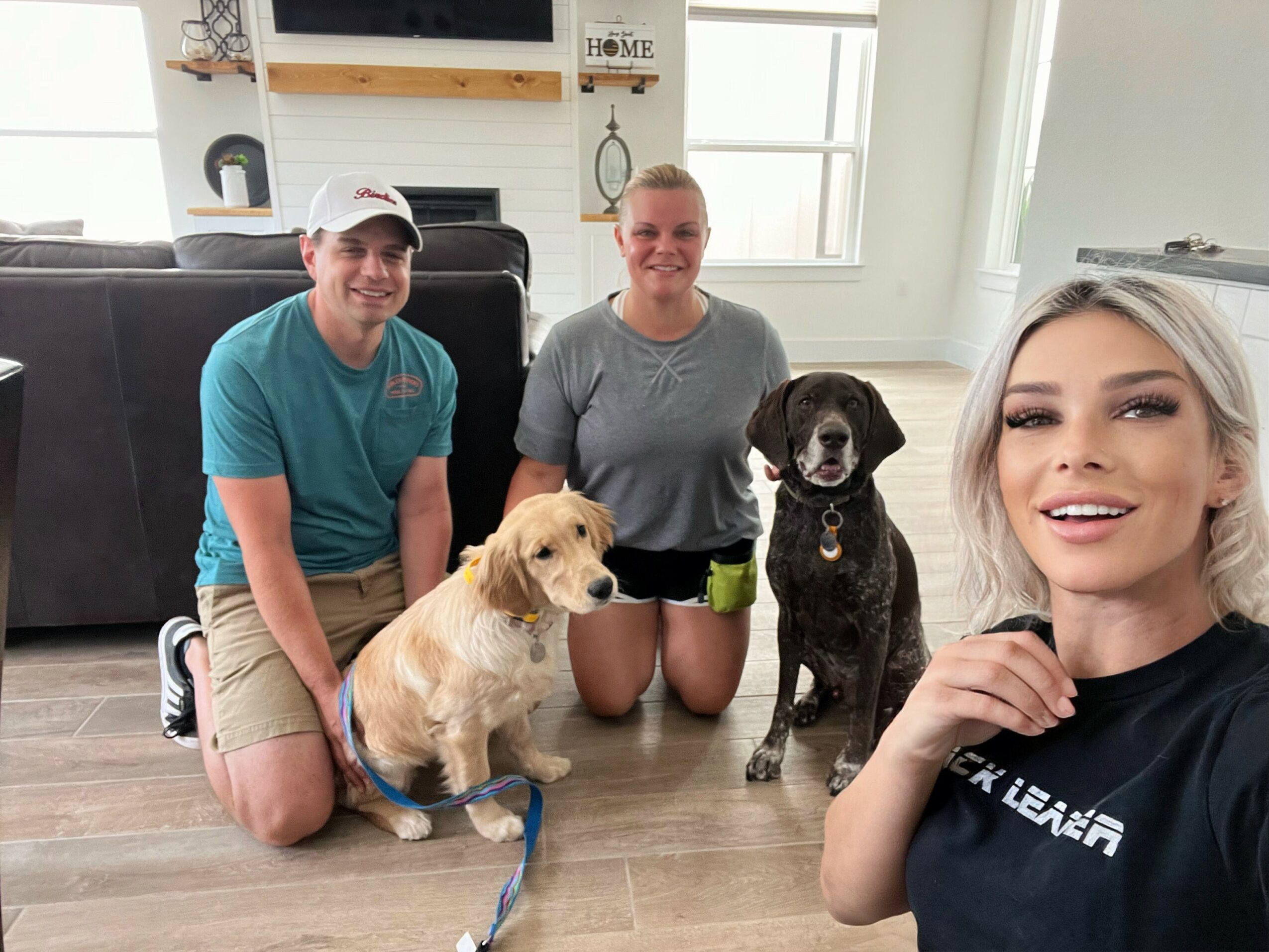 Three people and two dogs in a living room, smiling at the camera.
