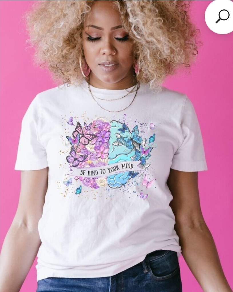 Woman with curly blonde hair wearing a white T-shirt with colorful butterfly design and text, standing against pink background.