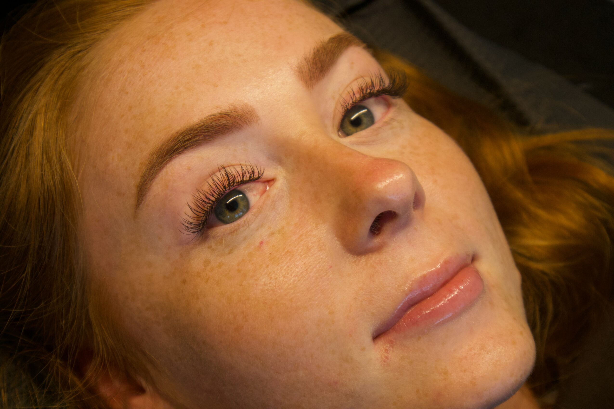 Close-up of a young woman with red hair, freckles, and makeup, looking slightly upward and to the side.