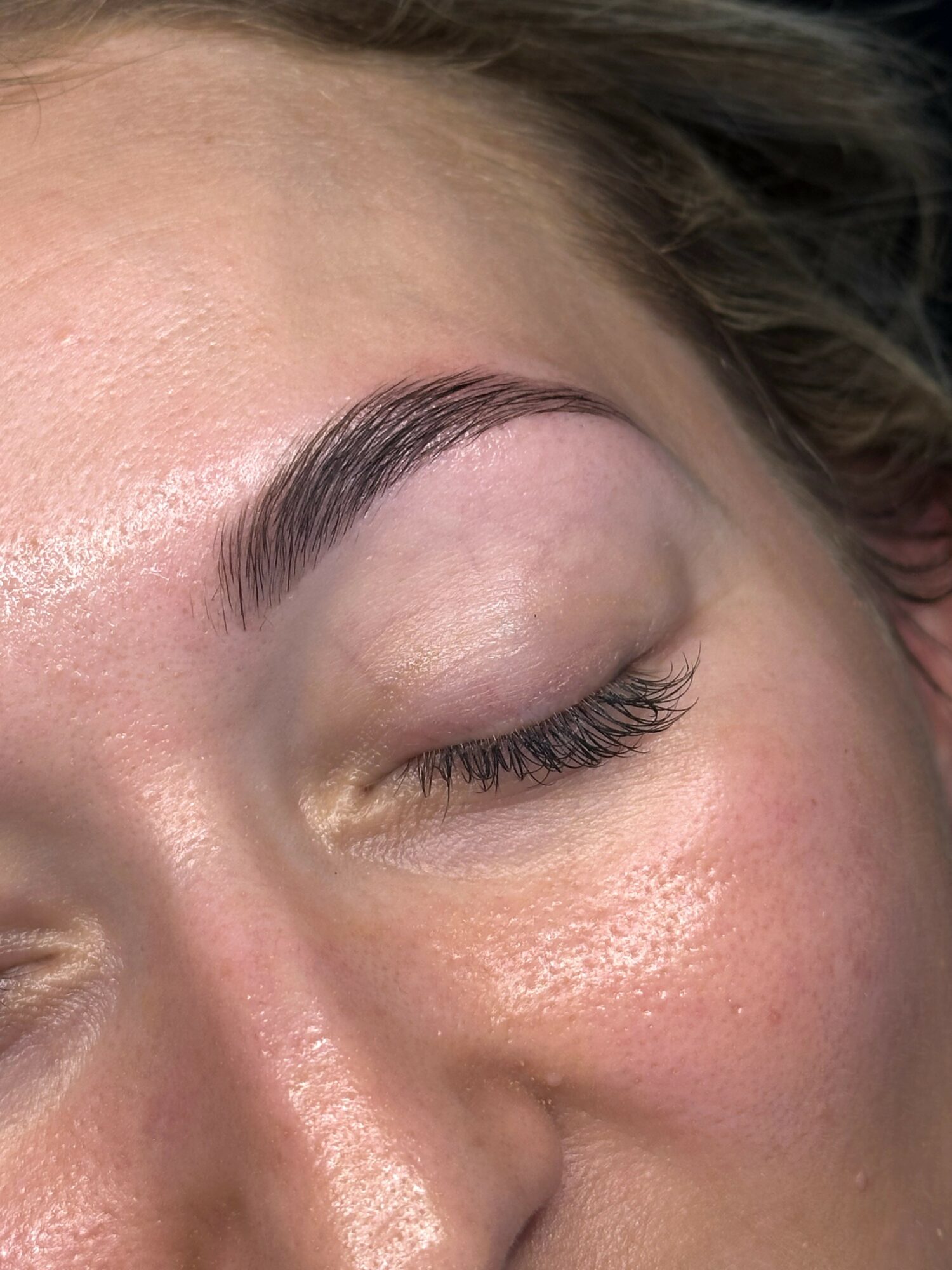Close-up of a person's face with closed eye, showing well-groomed eyebrow and smooth skin.