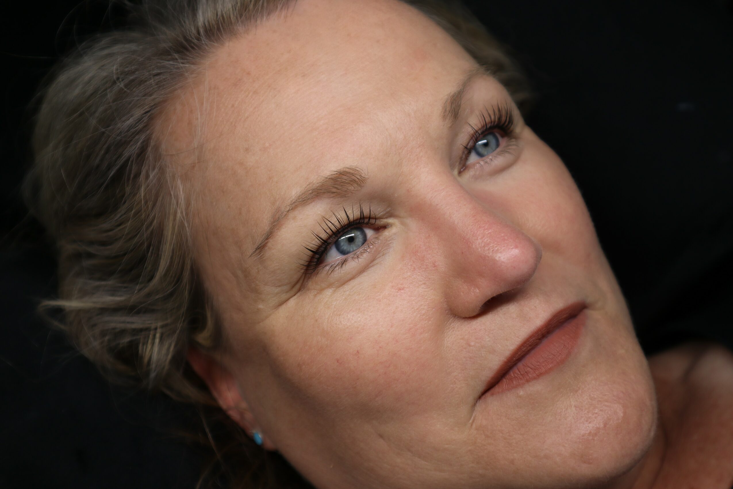 Close-up of a woman with light skin and blue eyes, looking upward with a slight smile.