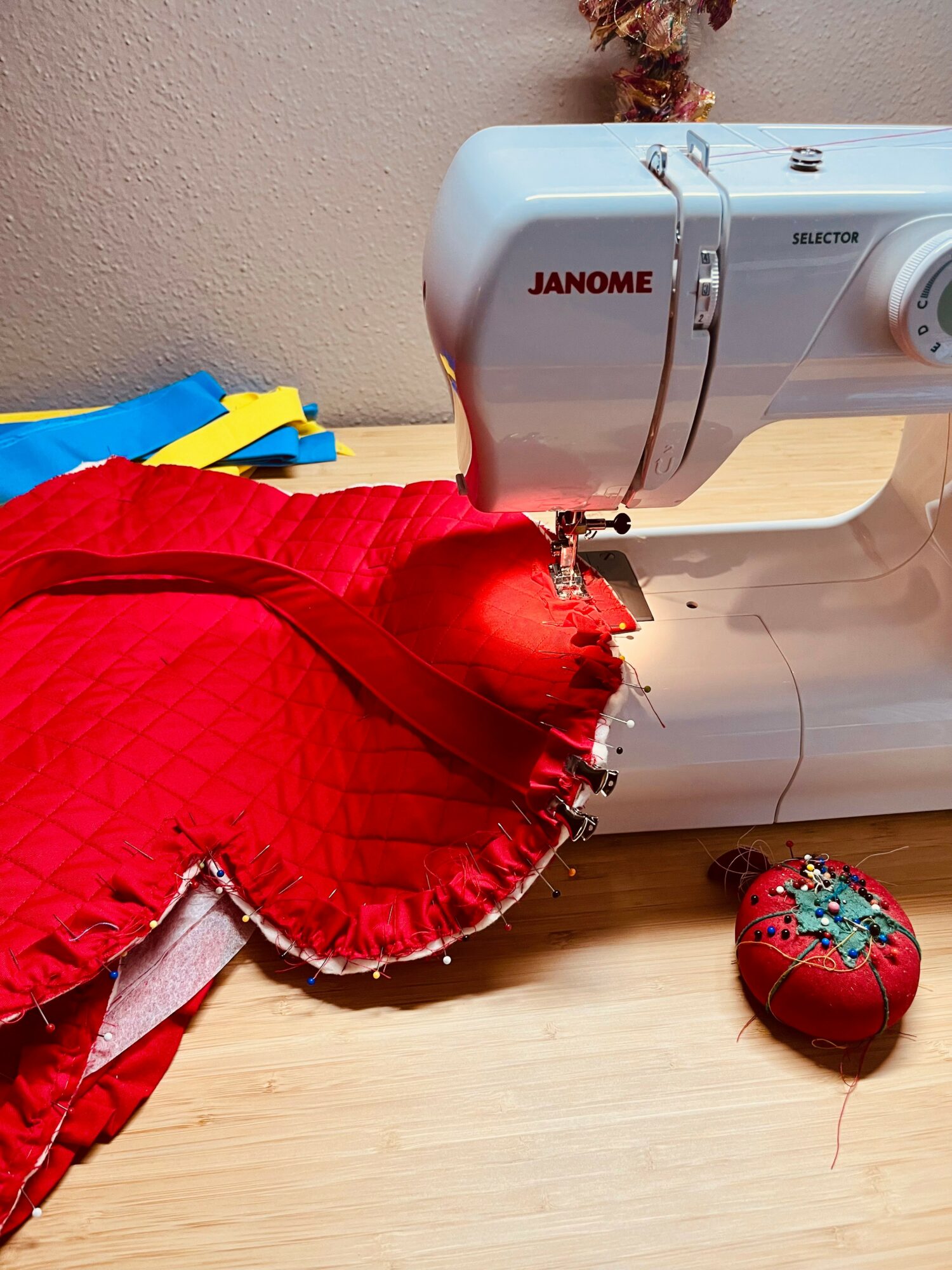 Sewing machine stitching red fabric with a heart-shaped object nearby on a wooden surface.