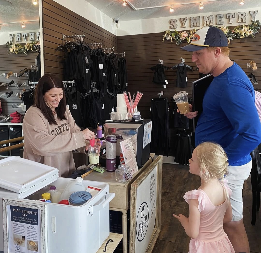 A woman at a checkout counter with a young girl and a man holding a drink, inside a store with clothing displays.