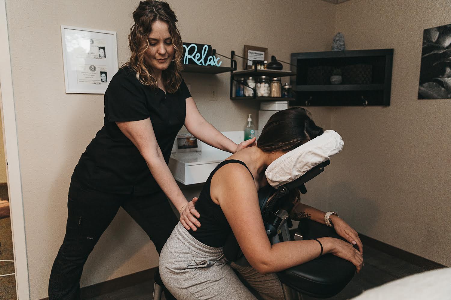 Woman receiving a massage from a therapist in a room with shelves and relaxation decor.