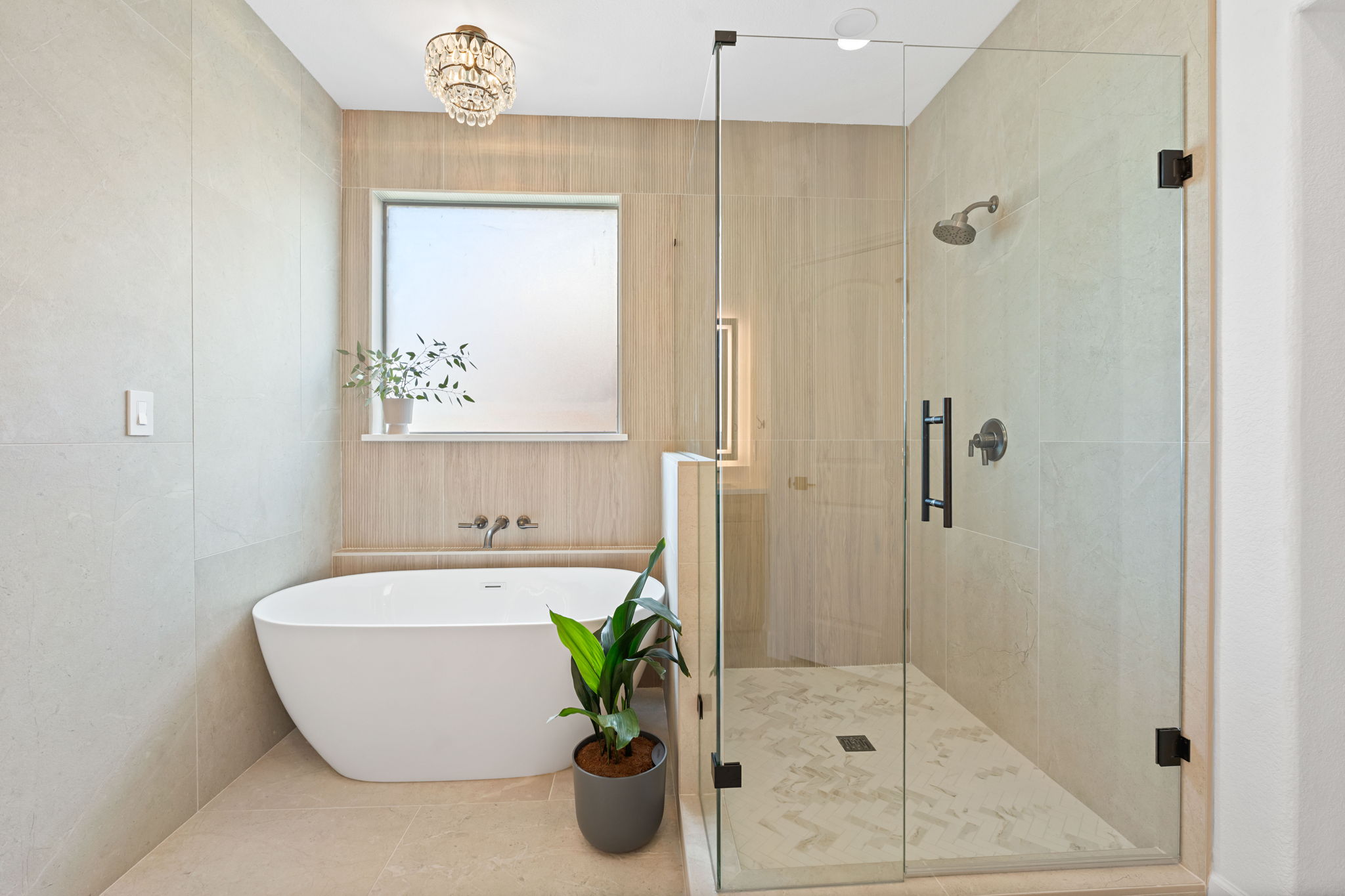 Bathroom with a freestanding bathtub, a glass shower enclosure, a window, and a small potted plant, neutral-colored walls.