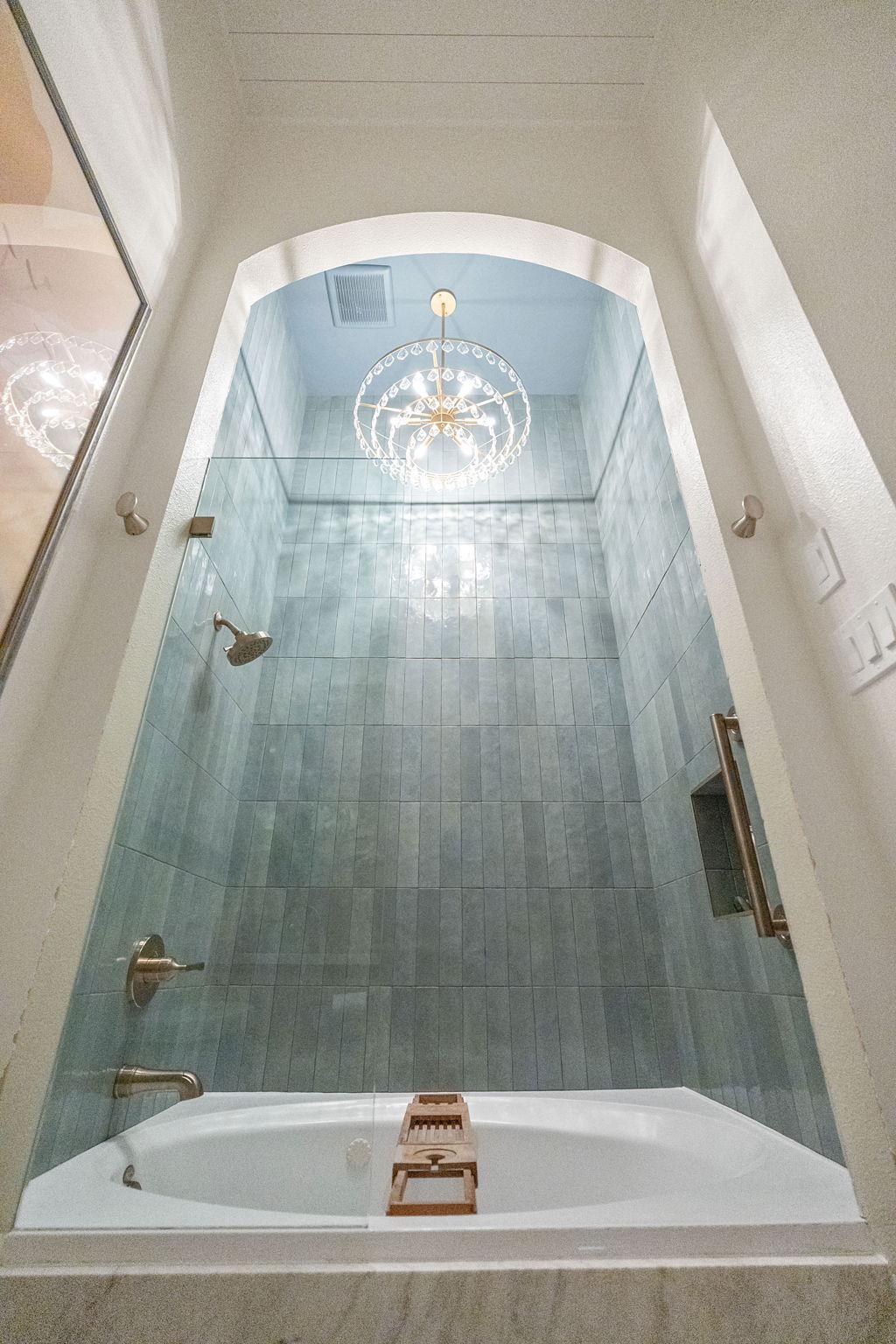 View of a shower with a chandelier reflection on the ceiling, seen from above, with a white bathtub at the bottom.