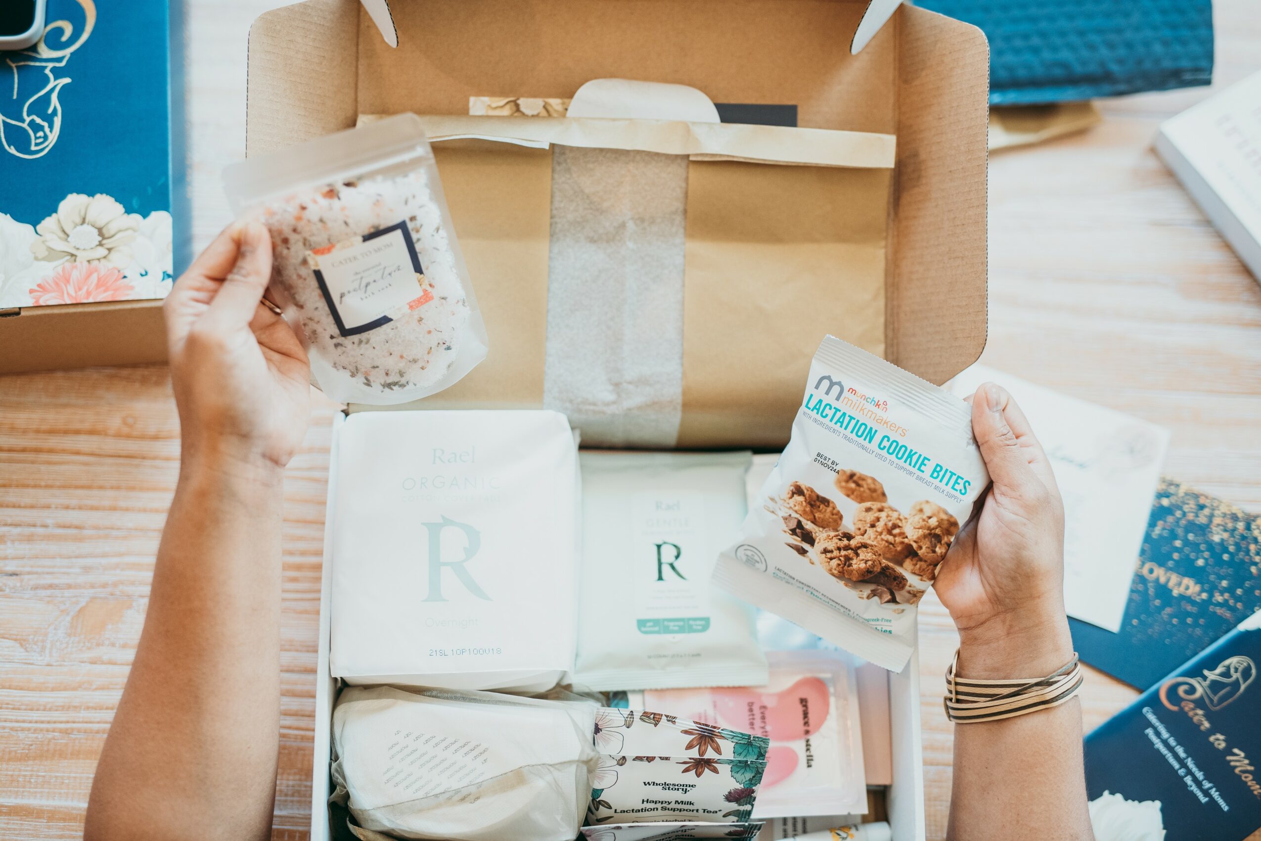 Two hands hold soap and a box of cereal above an open cardboard box on a wooden table.
