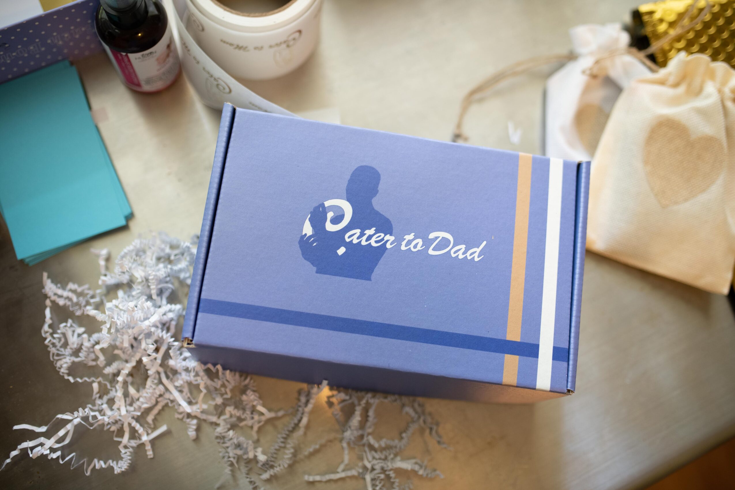 Blue gift box with white text reading 'A gift for Dad' on a table with various items nearby.