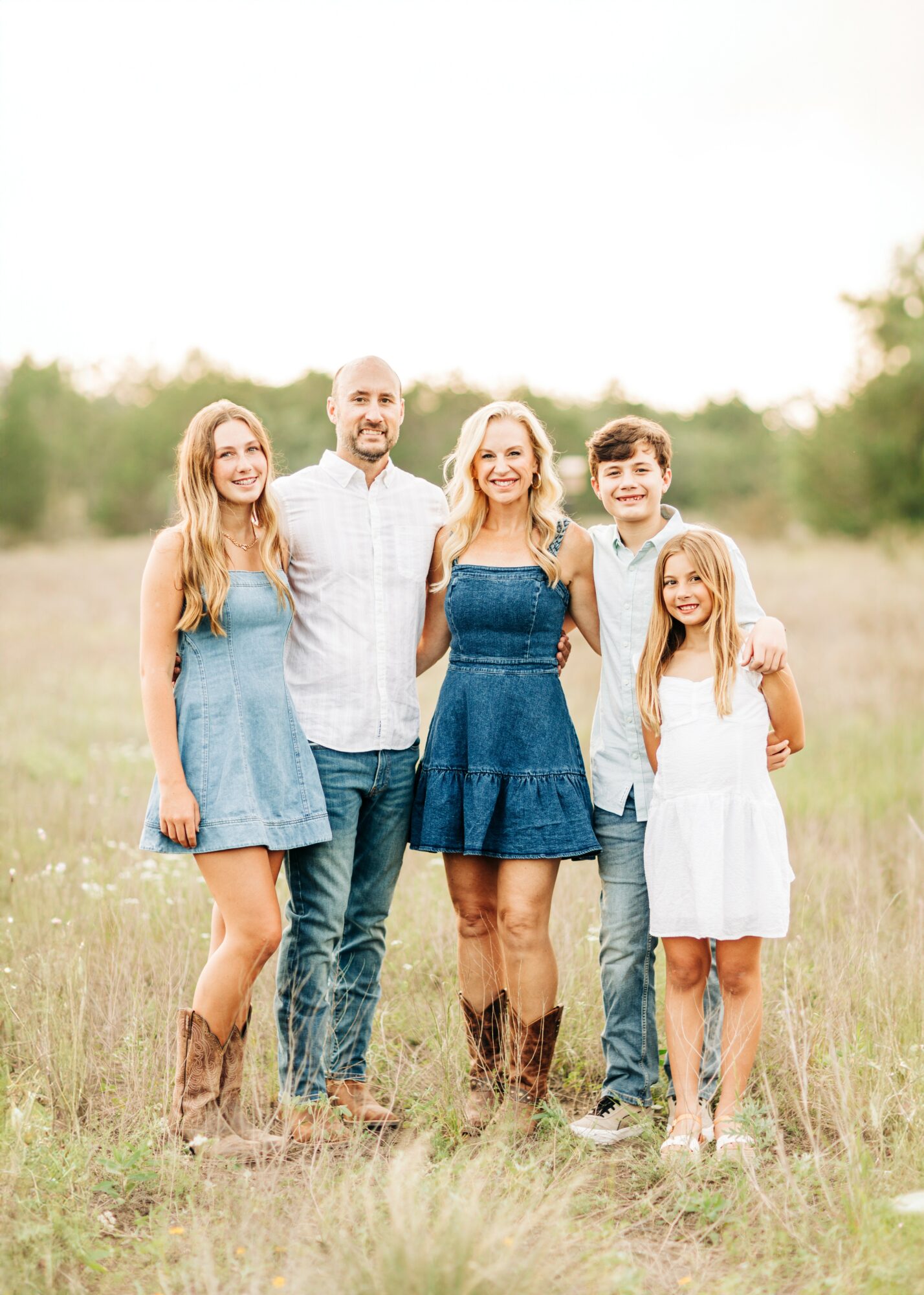 Group of five people standing outdoors in a grassy field, smiling, with trees in the background.