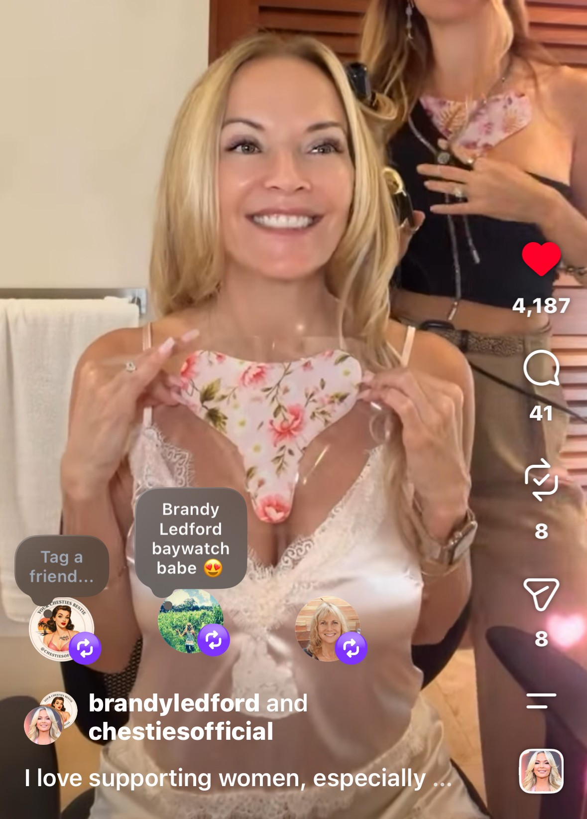 Smiling woman holding a floral face mask, with another person partially visible behind her, indoors.
