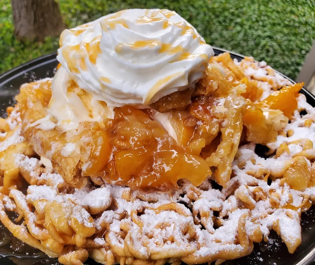 Close-up of a dessert with whipped cream, fruit filling, and powdered sugar on a dark plate outdoors.