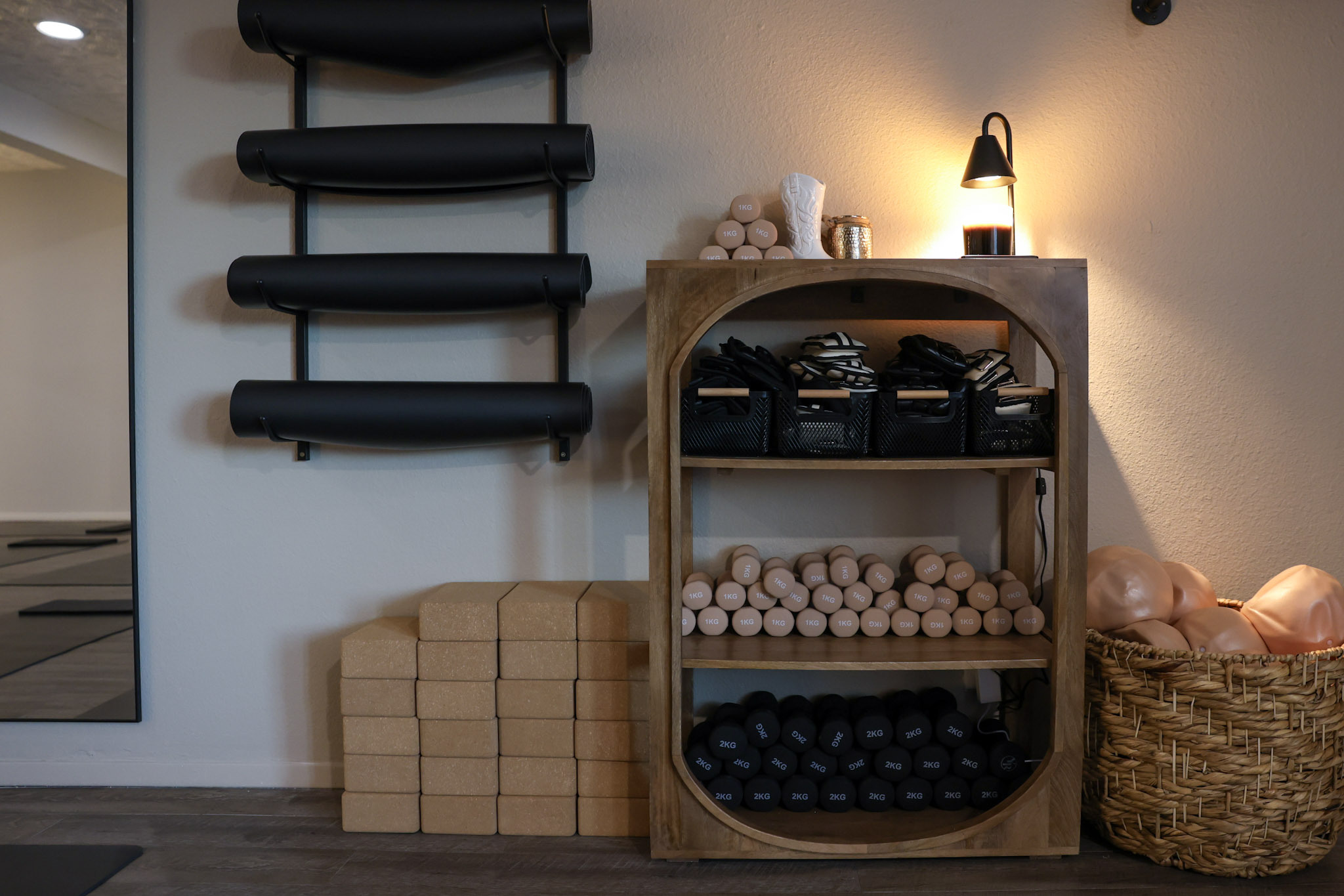 Wooden shelf with rolled towels, black storage boxes, and a lamp, next to a basket and stacked blocks, in a room.