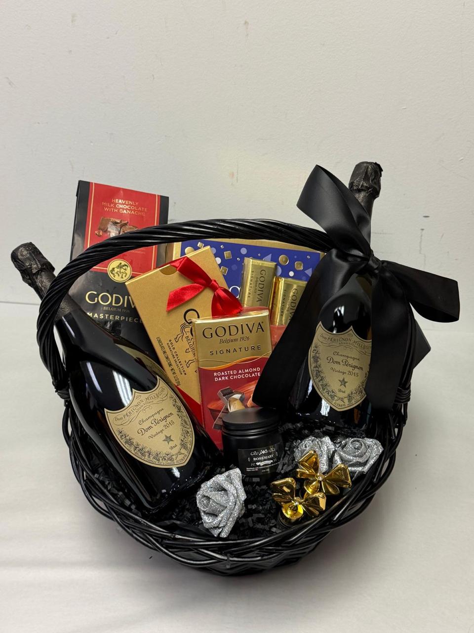 Black gift basket with chocolates, a gold bow, and a red and blue box inside, against a plain white background.