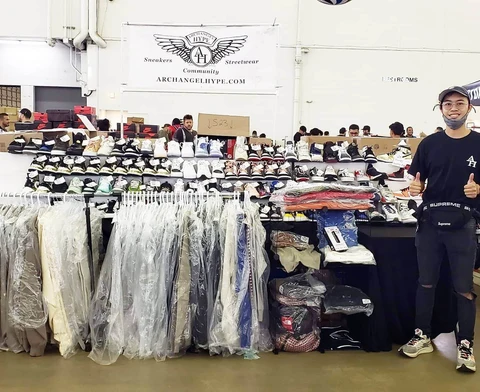 Person standing next to clothing racks and tables with various items in a warehouse or store setting.