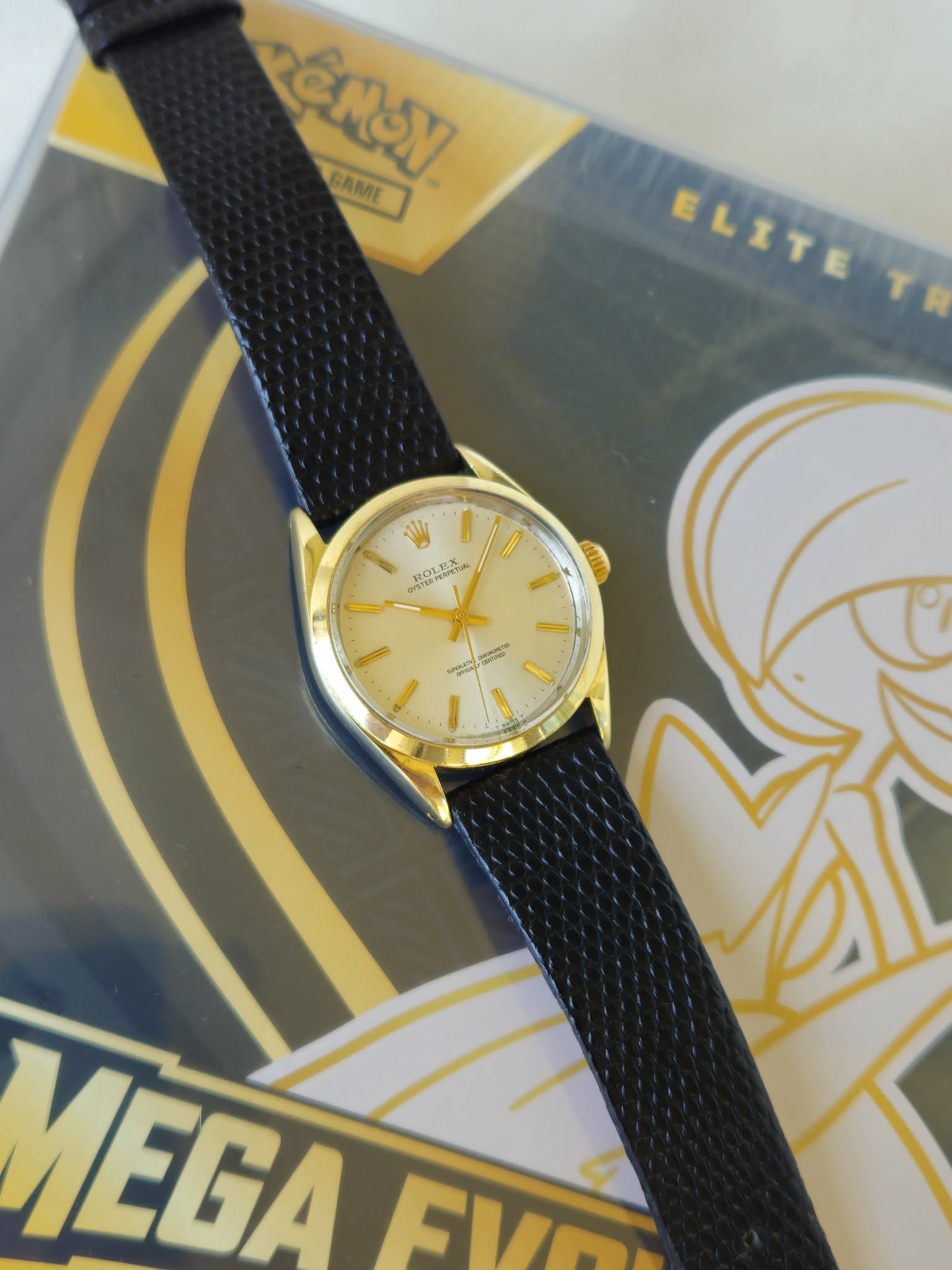 Gold watch with black strap resting on a comic book cover featuring a character in a helmet, yellow and black design elements.