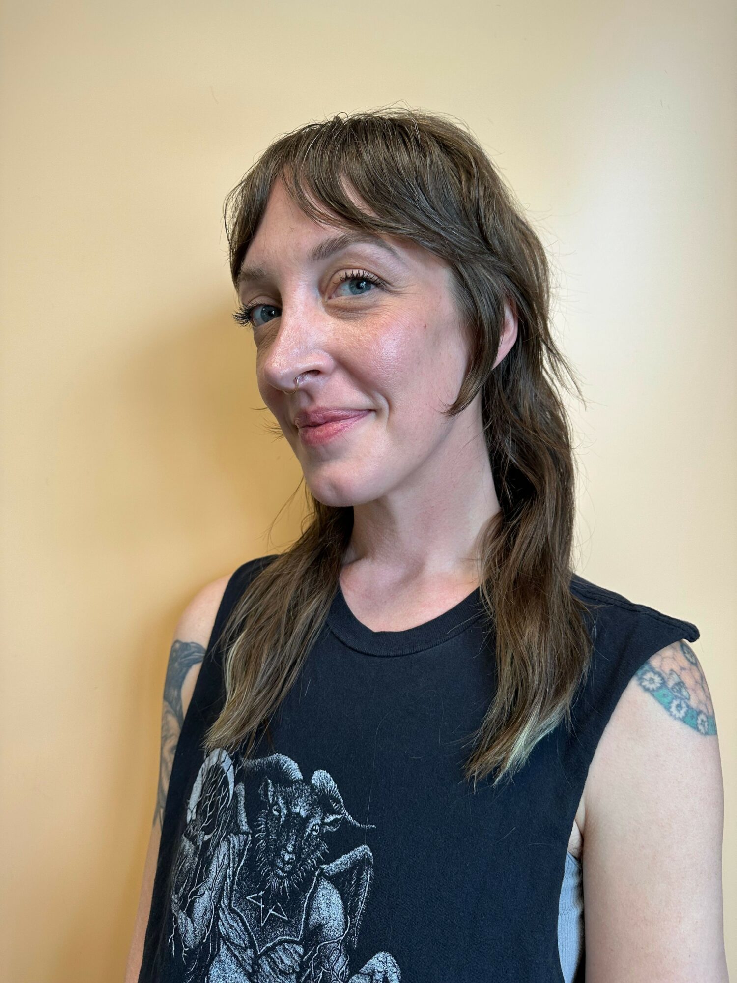 Young woman with long brown hair, wearing a black sleeveless top, smiling, against a plain background.
