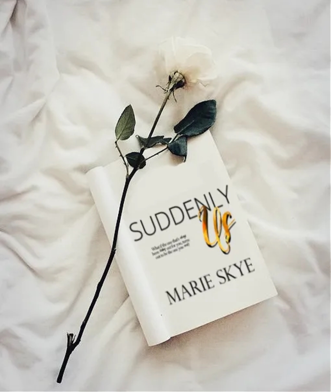 A white book titled 'Suddenly UC' by Marie Skye with a flower and leaves on top, placed on white fabric.