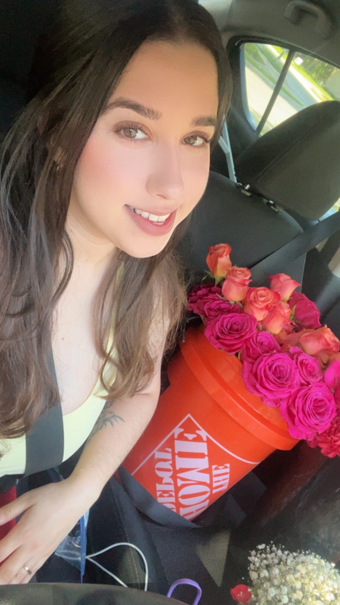 Young woman with long dark hair smiling in car next to a bucket of pink and purple roses, with a box of popcorn.