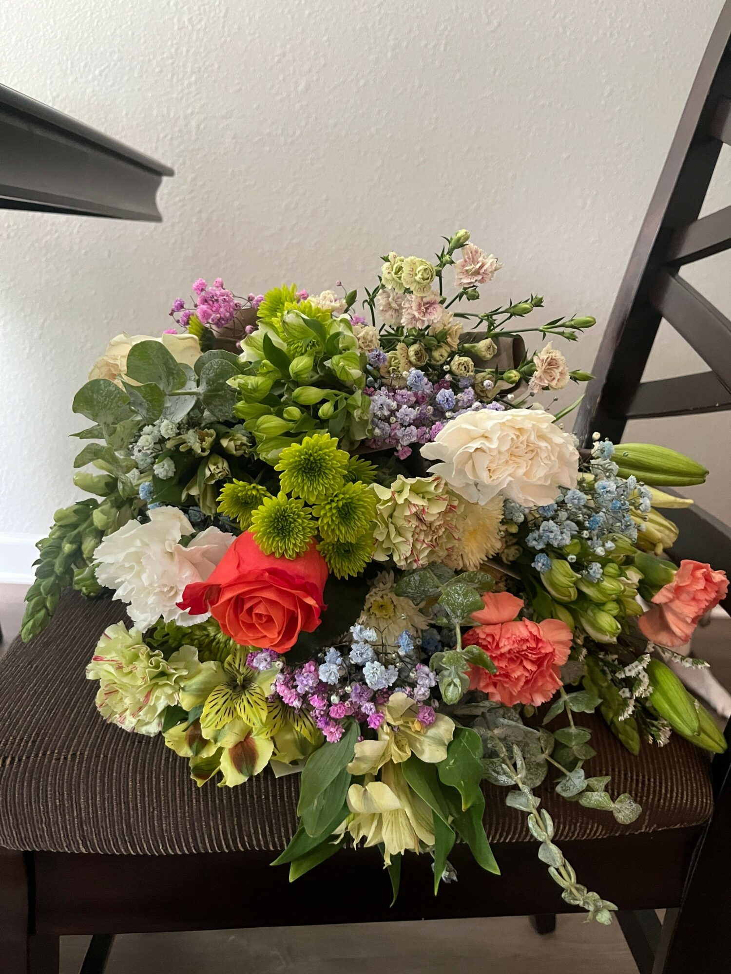 Colorful flower bouquet with roses, carnations, and greenery, arranged in a vase on a table.