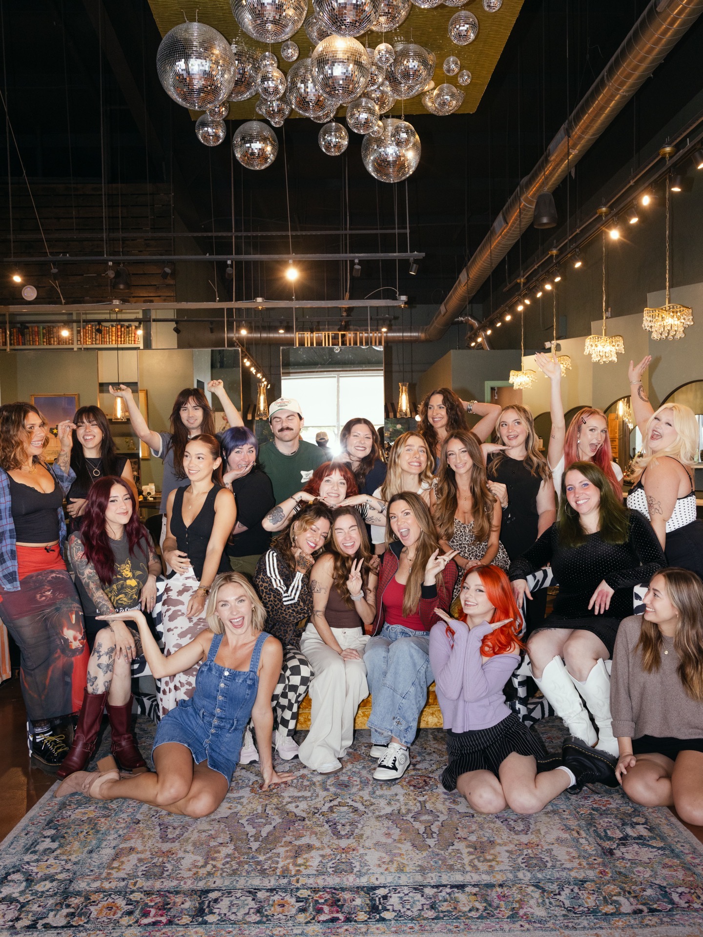 Group of women and a man posing in a decorated indoor space with hanging lights and a patterned rug.