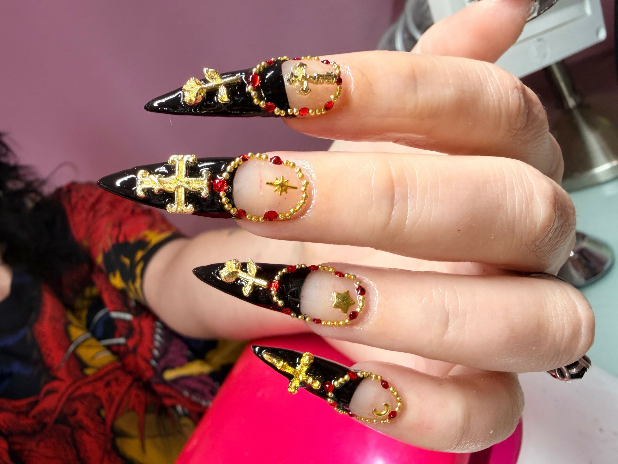 Close-up of decorated fingernails with black, gold, and red designs, including crosses and stars, on a person's hand.