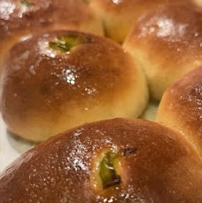 Close-up of baked bread rolls with shiny, golden-brown crust and green filling visible on top.