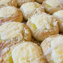 Close-up of baked bread rolls topped with cheese and herbs, some with melted cheese and crumbs, arranged closely together.