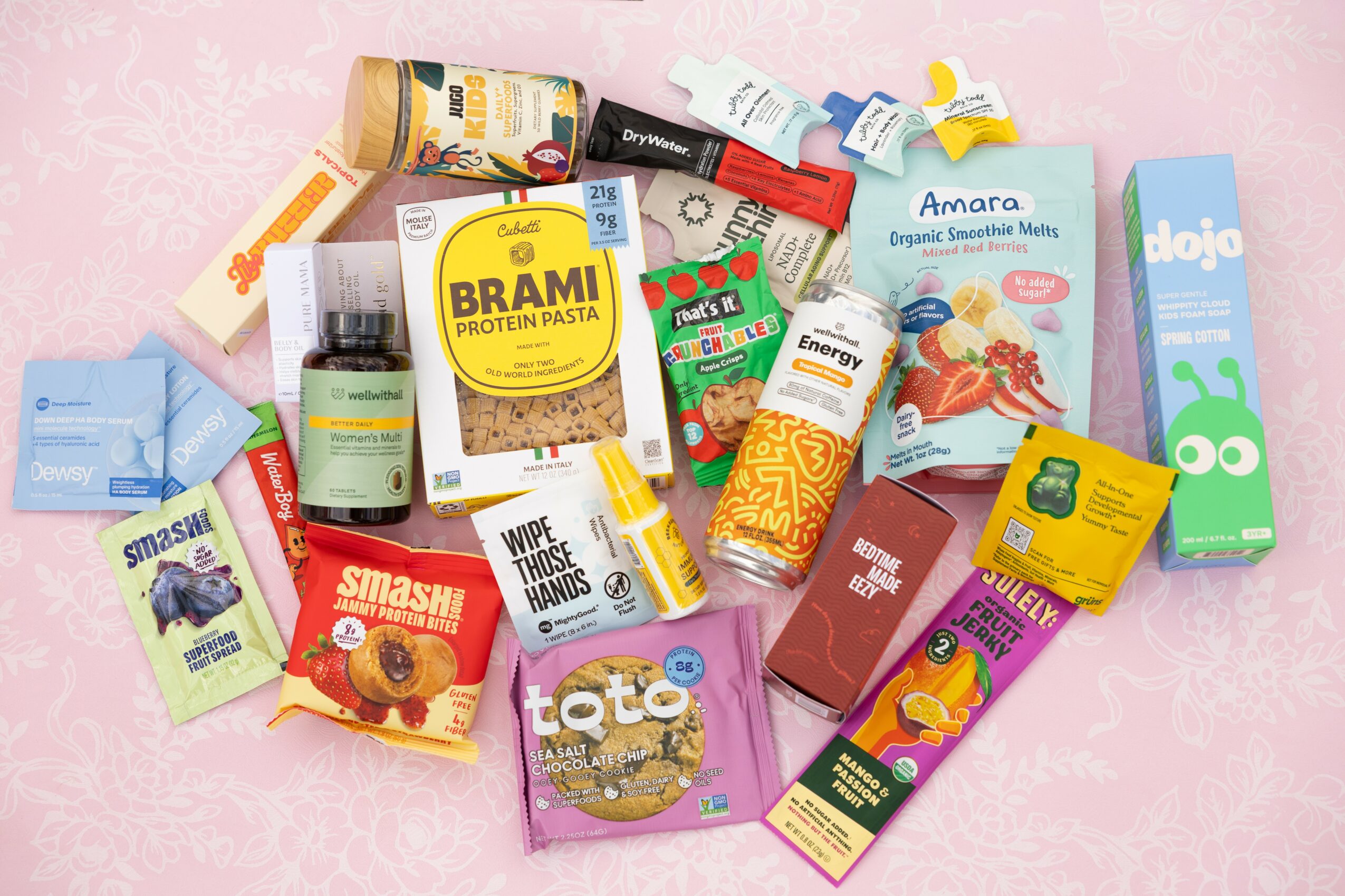Assorted snack and supplement packages scattered on a pink background.