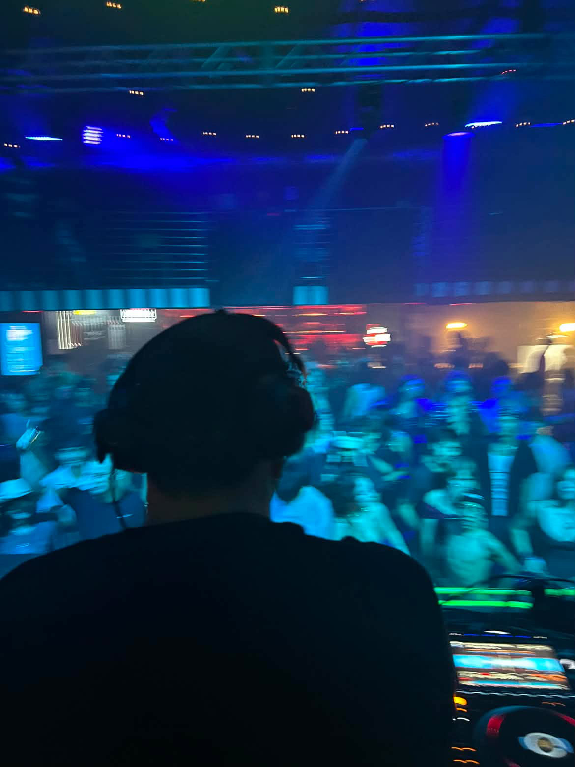 Person with headphones facing a large crowd at a concert or event, illuminated by blue and red lights.