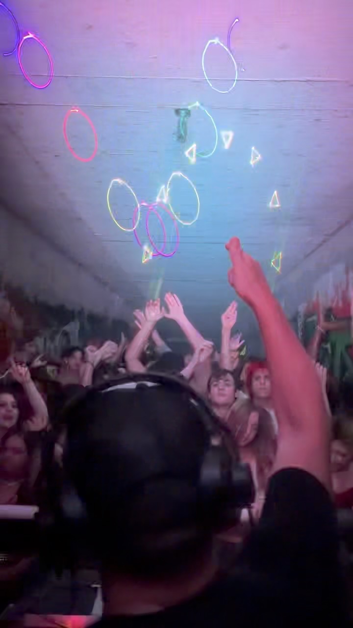 Crowd at a concert with hands raised, colorful lights and abstract shapes on the ceiling.