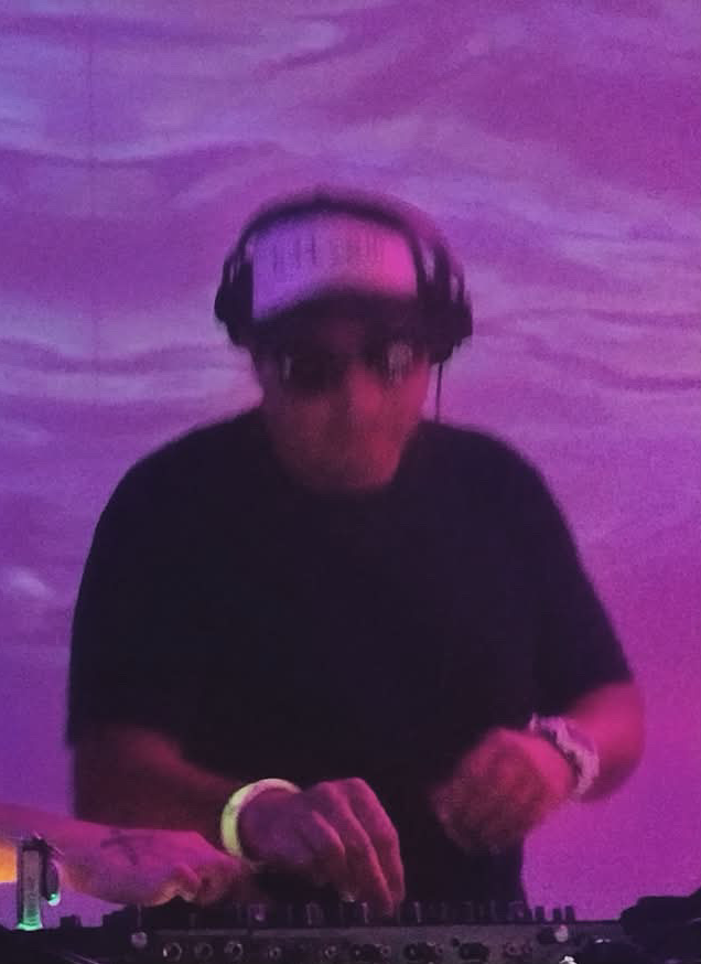 Person wearing headphones and sunglasses, operating DJ equipment against a purple background.